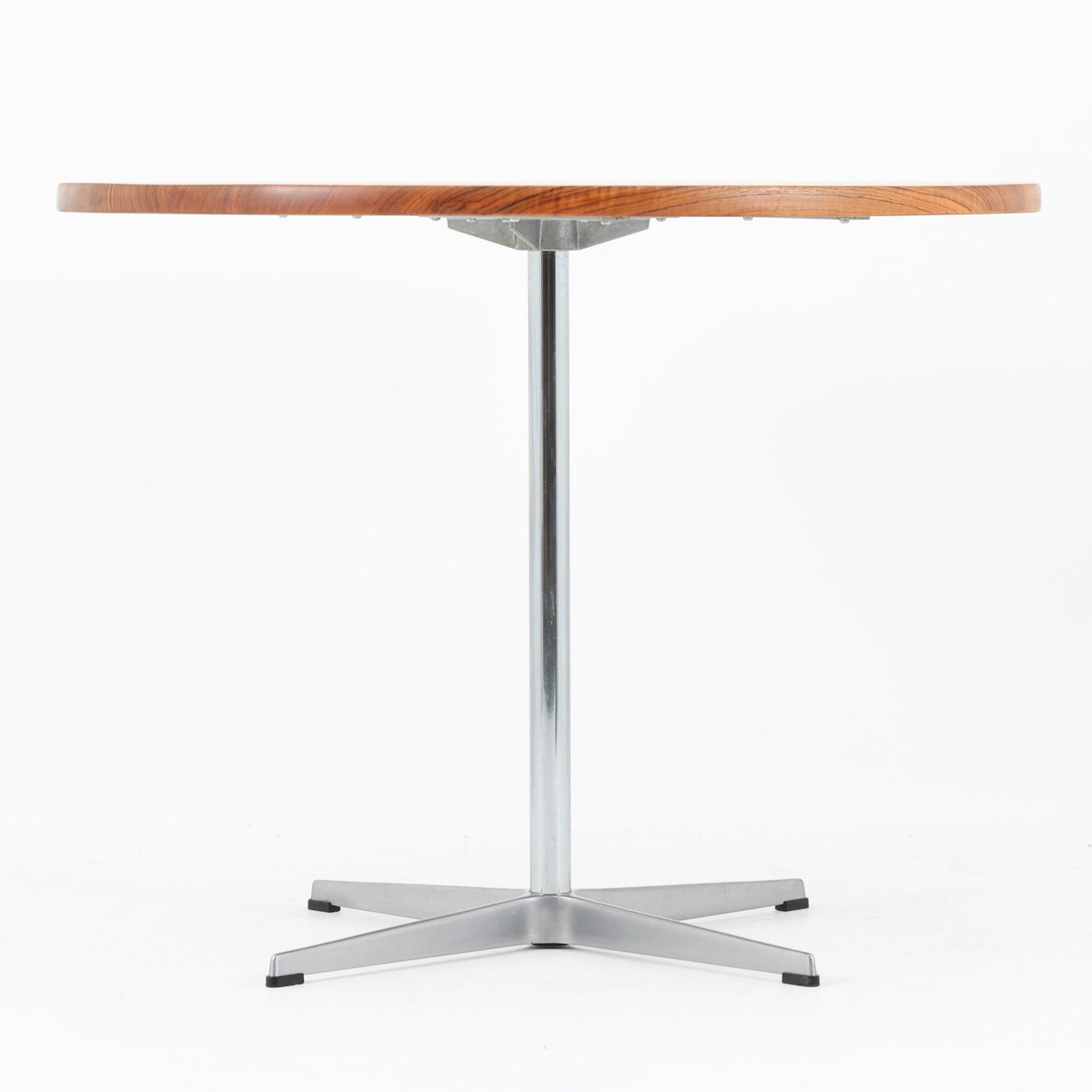 Arne Jacobsenがデザインし、Fritz Hansenが製作した円形ダイニングテーブルです。直径90cmのチーク無垢天板は、豊かな木目と滑らかな円形フォルムが美しく、空間に柔らかな印象をもたらします。シャープなスチール製の一本脚と4本スポークベースが軽快で洗練された佇まいを生み、ヤコブセンらしい機能美が際立つ一台。2～4人で使いやすいサイズ感で、ダイニングテーブルとしてはもちろん、カフェテーブルやラウンジ空間での打ち合わせ用テーブルとしてもおすすめです。中でもチーク無垢材仕様の個体は流通数が少なく珍しく、北欧ビンテージ市場でも希少性の高いモデルとして魅力を放ちます。経年により深みを増した木肌と無駄のない構造が、空間に上質な存在感を添えてくれます。