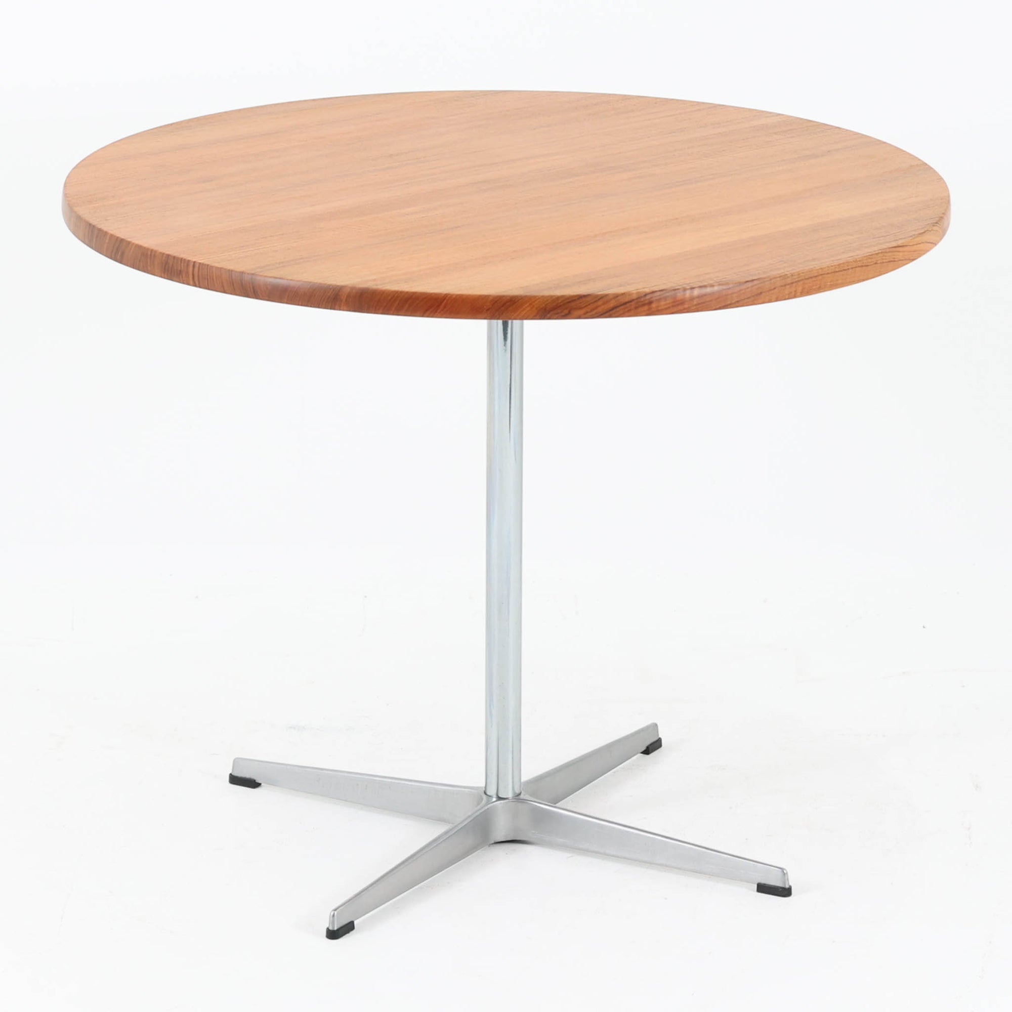 Arne Jacobsenがデザインし、Fritz Hansenが製作した円形ダイニングテーブルです。直径90cmのチーク無垢天板は、豊かな木目と滑らかな円形フォルムが美しく、空間に柔らかな印象をもたらします。シャープなスチール製の一本脚と4本スポークベースが軽快で洗練された佇まいを生み、ヤコブセンらしい機能美が際立つ一台。2～4人で使いやすいサイズ感で、ダイニングテーブルとしてはもちろん、カフェテーブルやラウンジ空間での打ち合わせ用テーブルとしてもおすすめです。中でもチーク無垢材仕様の個体は流通数が少なく珍しく、北欧ビンテージ市場でも希少性の高いモデルとして魅力を放ちます。経年により深みを増した木肌と無駄のない構造が、空間に上質な存在感を添えてくれます。