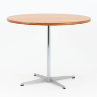 Arne Jacobsenがデザインし、Fritz Hansenが製作した円形ダイニングテーブルです。直径90cmのチーク無垢天板は、豊かな木目と滑らかな円形フォルムが美しく、空間に柔らかな印象をもたらします。シャープなスチール製の一本脚と4本スポークベースが軽快で洗練された佇まいを生み、ヤコブセンらしい機能美が際立つ一台。2～4人で使いやすいサイズ感で、ダイニングテーブルとしてはもちろん、カフェテーブルやラウンジ空間での打ち合わせ用テーブルとしてもおすすめです。中でもチーク無垢材仕様の個体は流通数が少なく珍しく、北欧ビンテージ市場でも希少性の高いモデルとして魅力を放ちます。経年により深みを増した木肌と無駄のない構造が、空間に上質な存在感を添えてくれます。