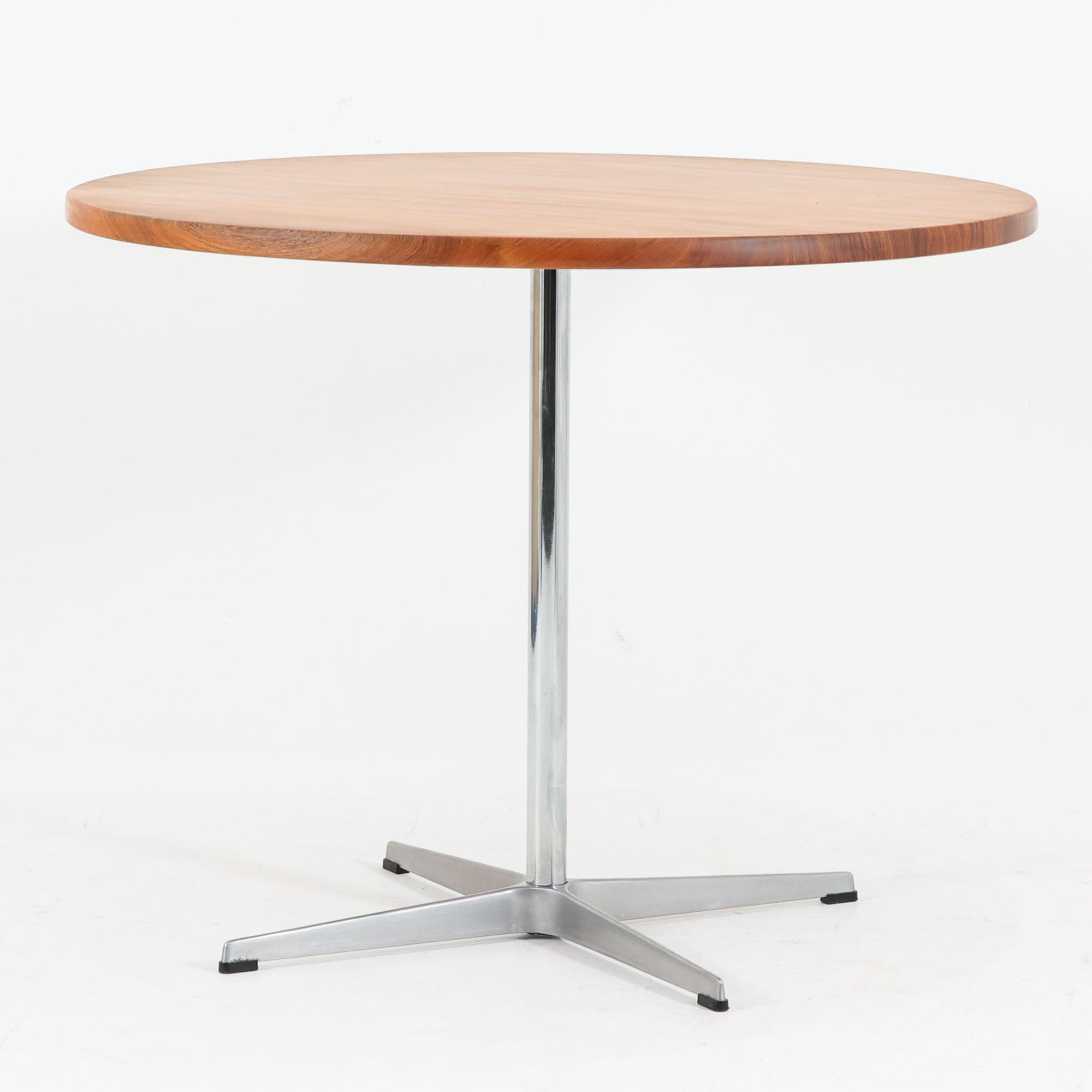 Arne Jacobsenがデザインし、Fritz Hansenが製作した円形ダイニングテーブルです。直径90cmのチーク無垢天板は、豊かな木目と滑らかな円形フォルムが美しく、空間に柔らかな印象をもたらします。シャープなスチール製の一本脚と4本スポークベースが軽快で洗練された佇まいを生み、ヤコブセンらしい機能美が際立つ一台。2～4人で使いやすいサイズ感で、ダイニングテーブルとしてはもちろん、カフェテーブルやラウンジ空間での打ち合わせ用テーブルとしてもおすすめです。中でもチーク無垢材仕様の個体は流通数が少なく珍しく、北欧ビンテージ市場でも希少性の高いモデルとして魅力を放ちます。経年により深みを増した木肌と無駄のない構造が、空間に上質な存在感を添えてくれます。