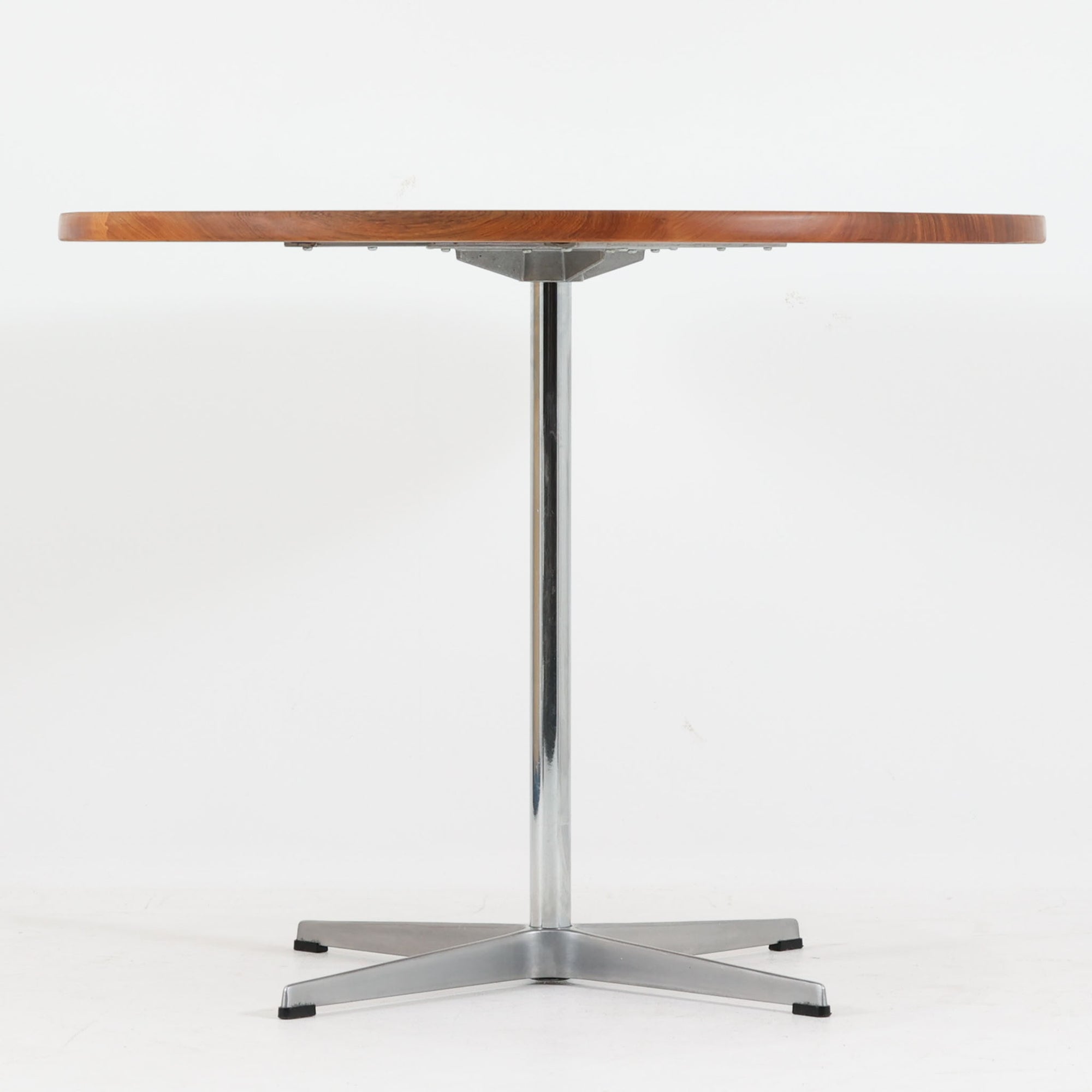 Arne Jacobsenがデザインし、Fritz Hansenが製作した円形ダイニングテーブルです。直径90cmのチーク無垢天板は、豊かな木目と滑らかな円形フォルムが美しく、空間に柔らかな印象をもたらします。シャープなスチール製の一本脚と4本スポークベースが軽快で洗練された佇まいを生み、ヤコブセンらしい機能美が際立つ一台。2～4人で使いやすいサイズ感で、ダイニングテーブルとしてはもちろん、カフェテーブルやラウンジ空間での打ち合わせ用テーブルとしてもおすすめです。中でもチーク無垢材仕様の個体は流通数が少なく珍しく、北欧ビンテージ市場でも希少性の高いモデルとして魅力を放ちます。経年により深みを増した木肌と無駄のない構造が、空間に上質な存在感を添えてくれます。