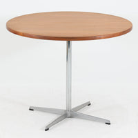 Arne Jacobsenがデザインし、Fritz Hansenが製作した円形ダイニングテーブルです。直径90cmのチーク無垢天板は、豊かな木目と滑らかな円形フォルムが美しく、空間に柔らかな印象をもたらします。シャープなスチール製の一本脚と4本スポークベースが軽快で洗練された佇まいを生み、ヤコブセンらしい機能美が際立つ一台。2～4人で使いやすいサイズ感で、ダイニングテーブルとしてはもちろん、カフェテーブルやラウンジ空間での打ち合わせ用テーブルとしてもおすすめです。中でもチーク無垢材仕様の個体は流通数が少なく珍しく、北欧ビンテージ市場でも希少性の高いモデルとして魅力を放ちます。経年により深みを増した木肌と無駄のない構造が、空間に上質な存在感を添えてくれます。
