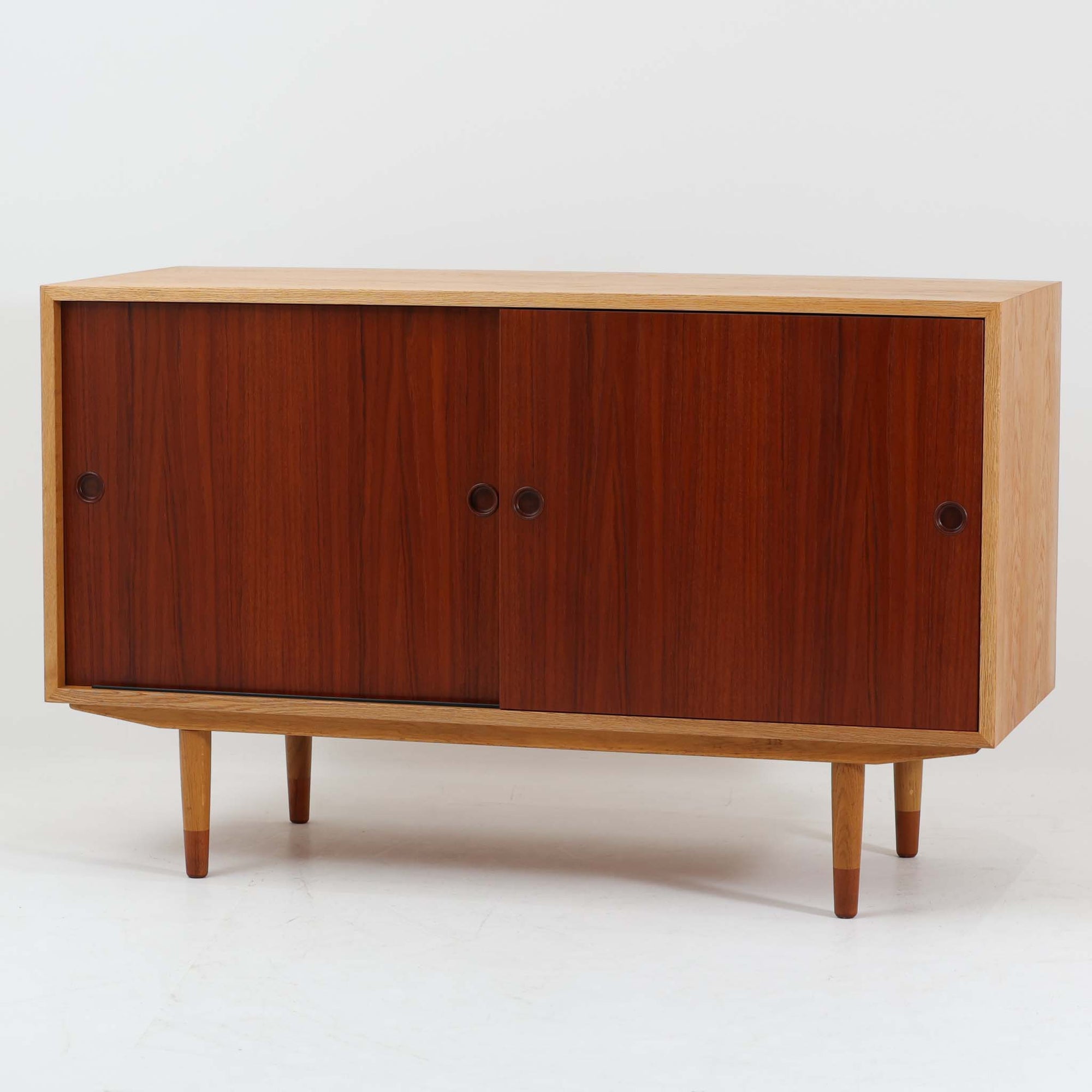 Borge Mogensenがデザインし、Karl Andersson & Sonerが製作したOresundシリーズのボードです。オーク材の明るく端正なフレームに、チーク材の引き戸を組み合わせたコントラストが美しく、モーエンセンらしい実用性と端正な佇まいが際立つ一台。幅135cmの扱いやすいサイズに、内部の棚板やトレー状の引き出しは可動式で、書類や雑誌、小物を用途に合わせて効率よく整理でき、リビング収納やテレビボード、サイドボードとして幅広く活躍します。さらに脚先にはオリジナルならではのチーク材ジョイントが備わり、細部にまで意匠性と実用性が感じられる希少な仕様も魅力。経年で深みを増した木肌と丁寧な木工技術、北欧オリジナルならではの希少性が空間に上質で知的な存在感を添えてくれます。