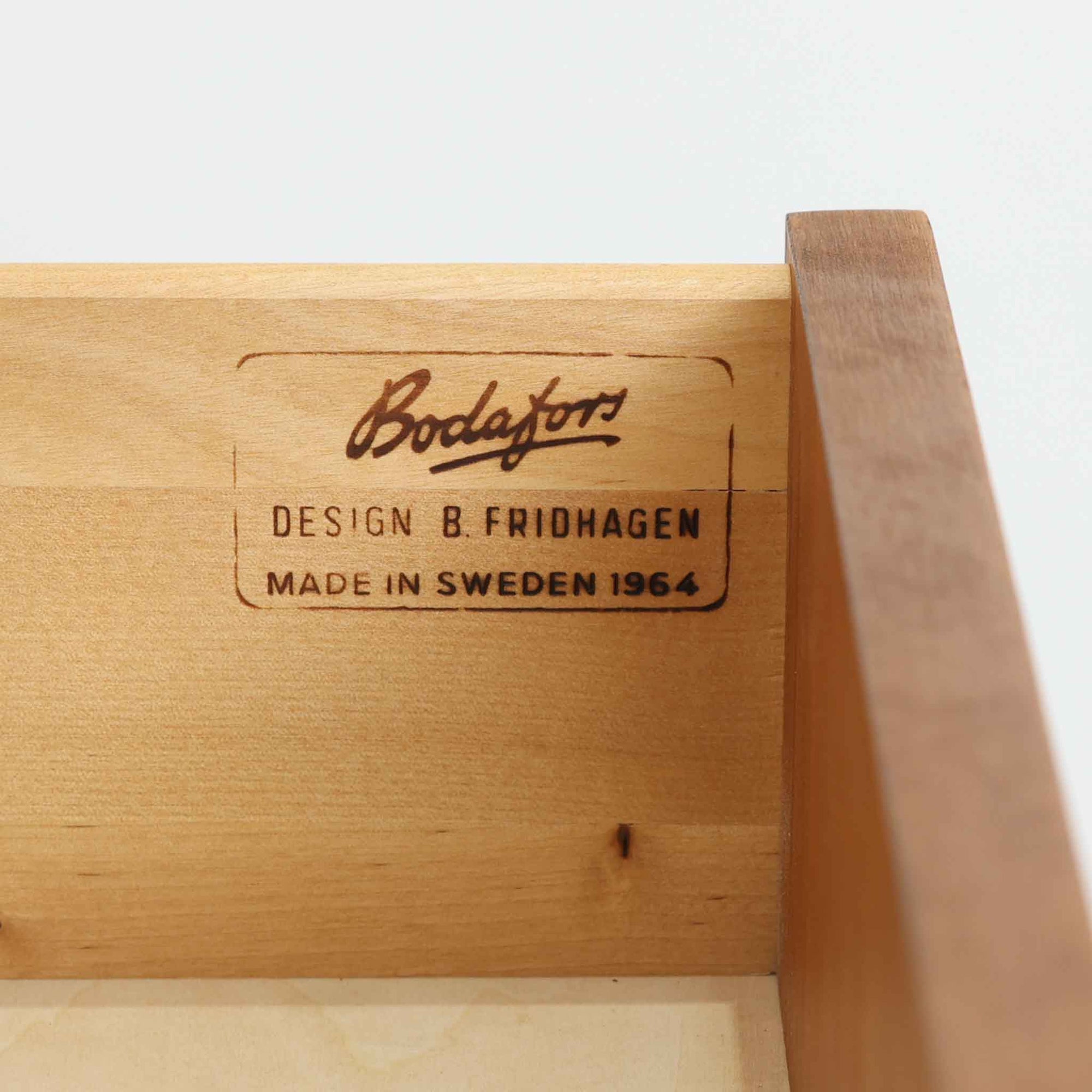 B. Fridhagenがデザインし、Bodaforsが製造したチーク材のディスプレイシェルフです。上部には背板のない開放的な棚を備え、書籍や器、オブジェなどを軽やかに飾れる構成。下部には4杯の引出しを組み合わせ、見せる収納と隠す収納を一台で使い分けられます。細身のフレームや直線的な脚部、縦に配した小ぶりな取手など、端正な職人技が感じられる佇まいも魅力。経年によって深みを増した木肌が、リビングや書斎、店舗空間に温かな存在感を添える一台です。