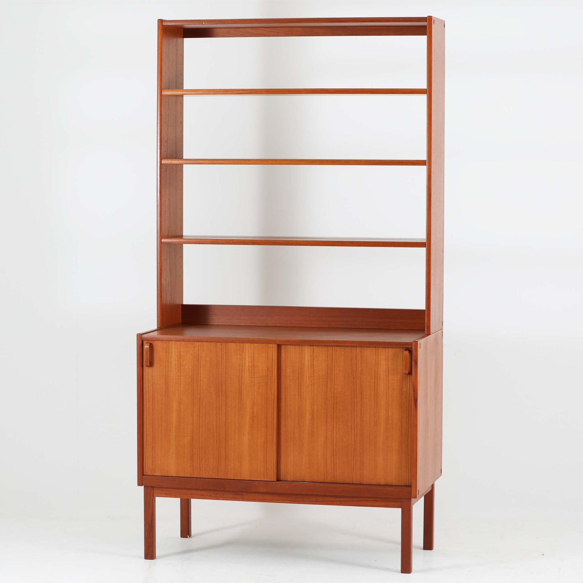 B. Fridhagenがデザインし、Bodaforsが製作したディスプレイシェルフです。チーク材ならではの美しい木目と経年で深みを増した艶やかな色合いが魅力で、上部のオープン棚と下部の引き戸収納を組み合わせた実用性の高い構成が北欧らしい機能美を感じさせます。幅90cmのすっきりとしたサイズは、書籍やオブジェ、器のディスプレイはもちろん、リビングや書斎での見せる収納と隠す収納を両立。細身の脚部が軽やかな印象を添え、Bodaforsらしい丁寧な木工技術とビンテージならではの希少性が空間に上質な存在感をもたらします。