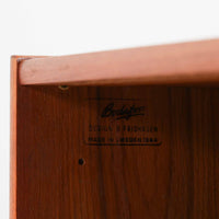 B. Fridhagenがデザインし、Bodaforsが製作したディスプレイシェルフです。チーク材ならではの美しい木目と経年で深みを増した艶やかな色合いが魅力で、上部のオープン棚と下部の引き戸収納を組み合わせた実用性の高い構成が北欧らしい機能美を感じさせます。幅90cmのすっきりとしたサイズは、書籍やオブジェ、器のディスプレイはもちろん、リビングや書斎での見せる収納と隠す収納を両立。細身の脚部が軽やかな印象を添え、Bodaforsらしい丁寧な木工技術とビンテージならではの希少性が空間に上質な存在感をもたらします。