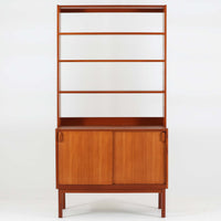 B. Fridhagenがデザインし、Bodaforsが製作したディスプレイシェルフです。チーク材ならではの美しい木目と経年で深みを増した艶やかな色合いが魅力で、上部のオープン棚と下部の引き戸収納を組み合わせた実用性の高い構成が北欧らしい機能美を感じさせます。幅90cmのすっきりとしたサイズは、書籍やオブジェ、器のディスプレイはもちろん、リビングや書斎での見せる収納と隠す収納を両立。細身の脚部が軽やかな印象を添え、Bodaforsらしい丁寧な木工技術とビンテージならではの希少性が空間に上質な存在感をもたらします。