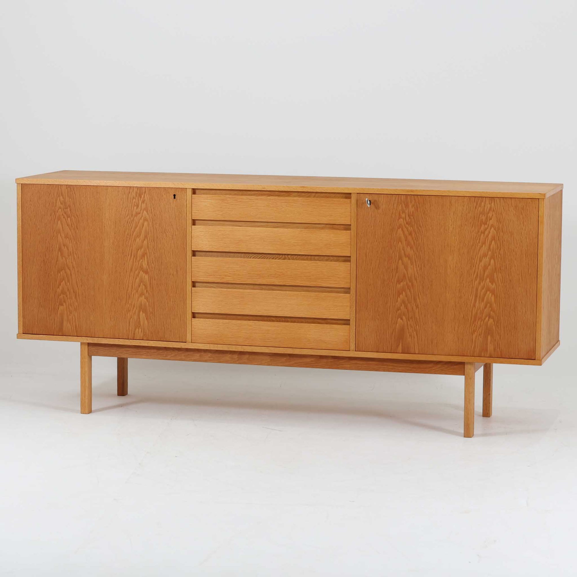 スウェーデン製収納キャビネットです。オーク材ならではの美しい木目と明るく上品な色合いが空間に軽やかな温もりを添え、幅180cmのワイドなサイズが高い収納力を実現します。中央の5段引き出しに加え、左右の扉内には棚板を備え、書類やカトラリー、リビング小物まで用途に応じて整理しやすい実用的な構成。細身の脚部が全体に抜け感を与え、北欧らしいミニマルで端正な佇まいが魅力です。リビングのサイドボードやダイニングでの収納家具としてはもちろん、ショップ什器としても映える、ビンテージならではの希少性と丁寧な木工技術を感じられる一台です。