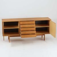 スウェーデン製収納キャビネットです。オーク材ならではの美しい木目と明るく上品な色合いが空間に軽やかな温もりを添え、幅180cmのワイドなサイズが高い収納力を実現します。中央の5段引き出しに加え、左右の扉内には棚板を備え、書類やカトラリー、リビング小物まで用途に応じて整理しやすい実用的な構成。細身の脚部が全体に抜け感を与え、北欧らしいミニマルで端正な佇まいが魅力です。リビングのサイドボードやダイニングでの収納家具としてはもちろん、ショップ什器としても映える、ビンテージならではの希少性と丁寧な木工技術を感じられる一台です。