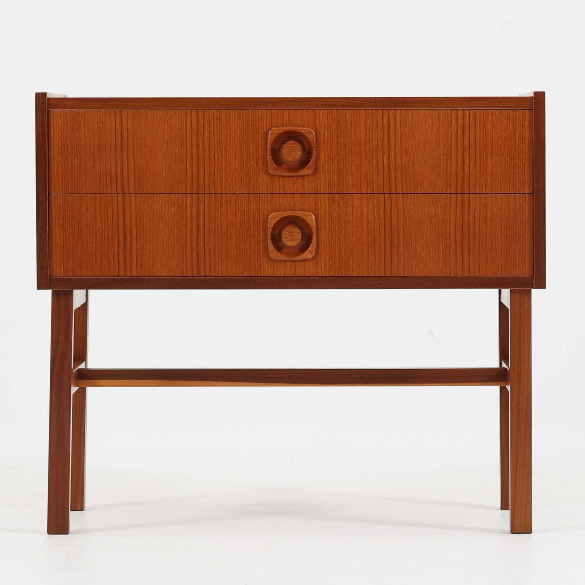 スウェーデン製チーク材2段チェストです。幅58cmの取り入れやすいサイズに、縦方向の美しい木目を活かした前板と印象的な円形の削り出し取っ手が映える、北欧らしい端正な一台。2杯の引き出しは衣類や日用品、小物をすっきり整理しやすく、ソファ横のサイドチェストやベッドサイドのナイトテーブルとしても活躍します。細身の脚部と貫が全体に軽やかな印象を与え、経年で深みを増したチークの艶やかな木肌が空間に上質な温もりを添えます。限られた空間にも置きやすく、ビンテージならではの丁寧な造りと希少性を楽しめる収納家具です。