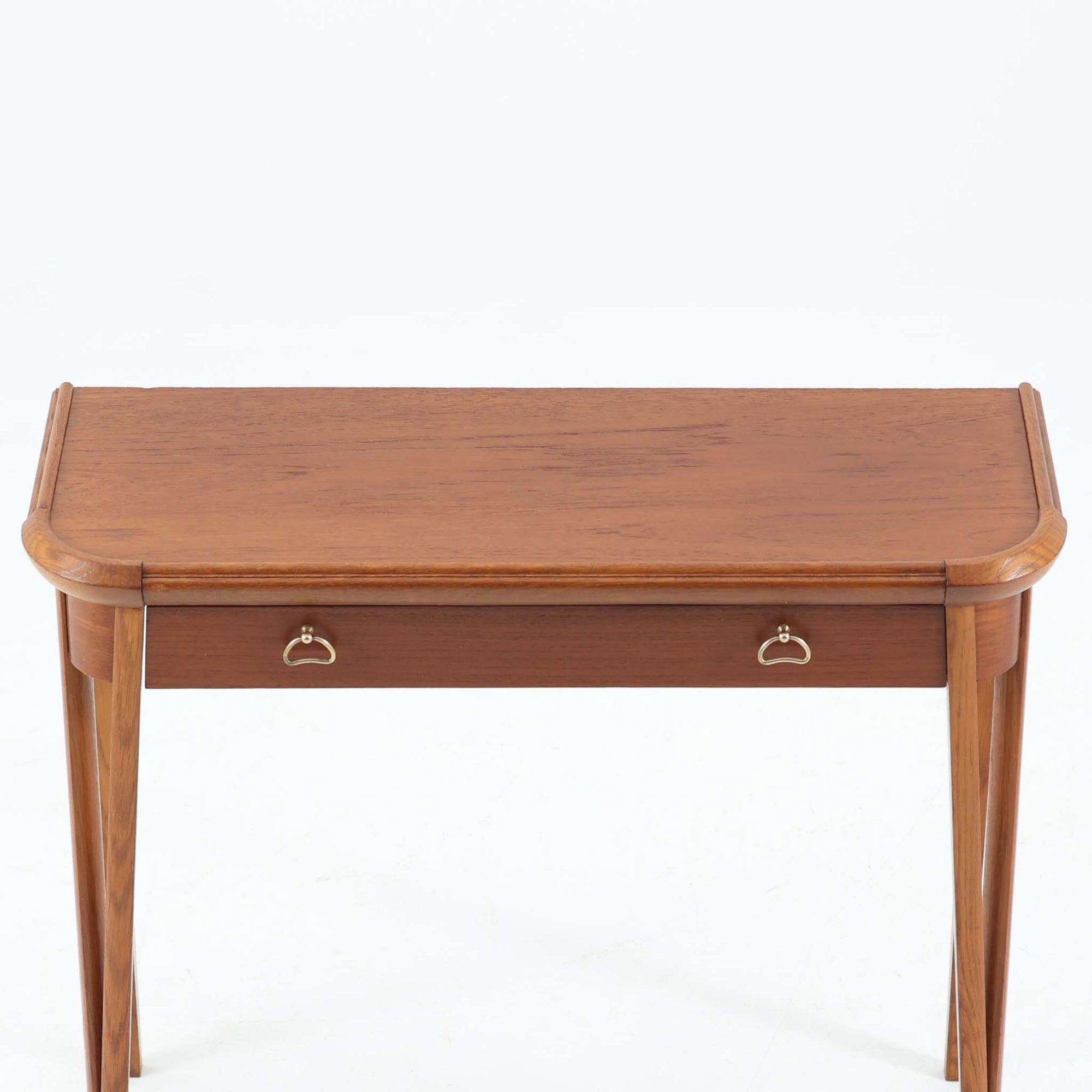 スウェーデンで製作されたコンソールテーブルです。天板にはチーク材、脚部にはオーク材を組み合わせ、温かみのある木目と落ち着いた色合いが北欧らしい上品な雰囲気を演出します。天板下には引き出しが備えられており、小物や文具などをすっきり収納できる実用的な構造。丸みを帯びた天板の角や細身のテーパー脚が軽やかな印象を与え、玄関やリビング、ベッドサイドなど限られたスペースにも収まりやすいサイズ感です。経年により深みを増した木部の表情が魅力の北欧ビンテージ家具です。