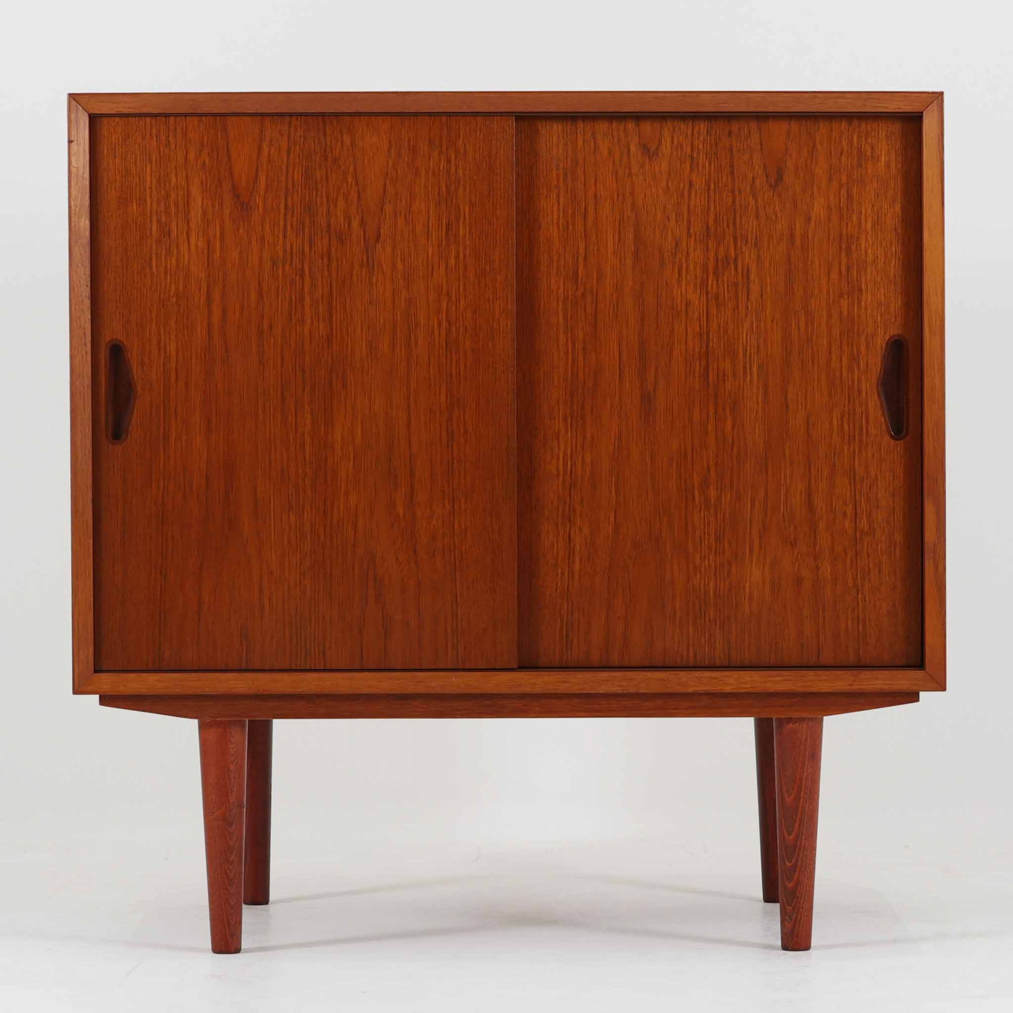 Olholm Mobelfabrik（オルホルム・モベルファブリック）によるデンマーク製のチーク材ボードです。幅80cmの取り入れやすいサイズに、すっきりとした引き戸と先細りの脚部を合わせた軽やかな佇まいが北欧らしい一台。内部は左右に棚板を備えた実用的な収納構造で、書籍や日用品、小物を整理しながら美しく収められます。経年により深みを増したチークの艶やかな木肌と、無駄を削ぎ落とした端正なフォルムが、リビングのサイドボードやベッドサイド収納として上質な存在感を演出。限られた空間にも置きやすく、ビンテージならではの丁寧な造りと希少性を楽しめる収納家具です。