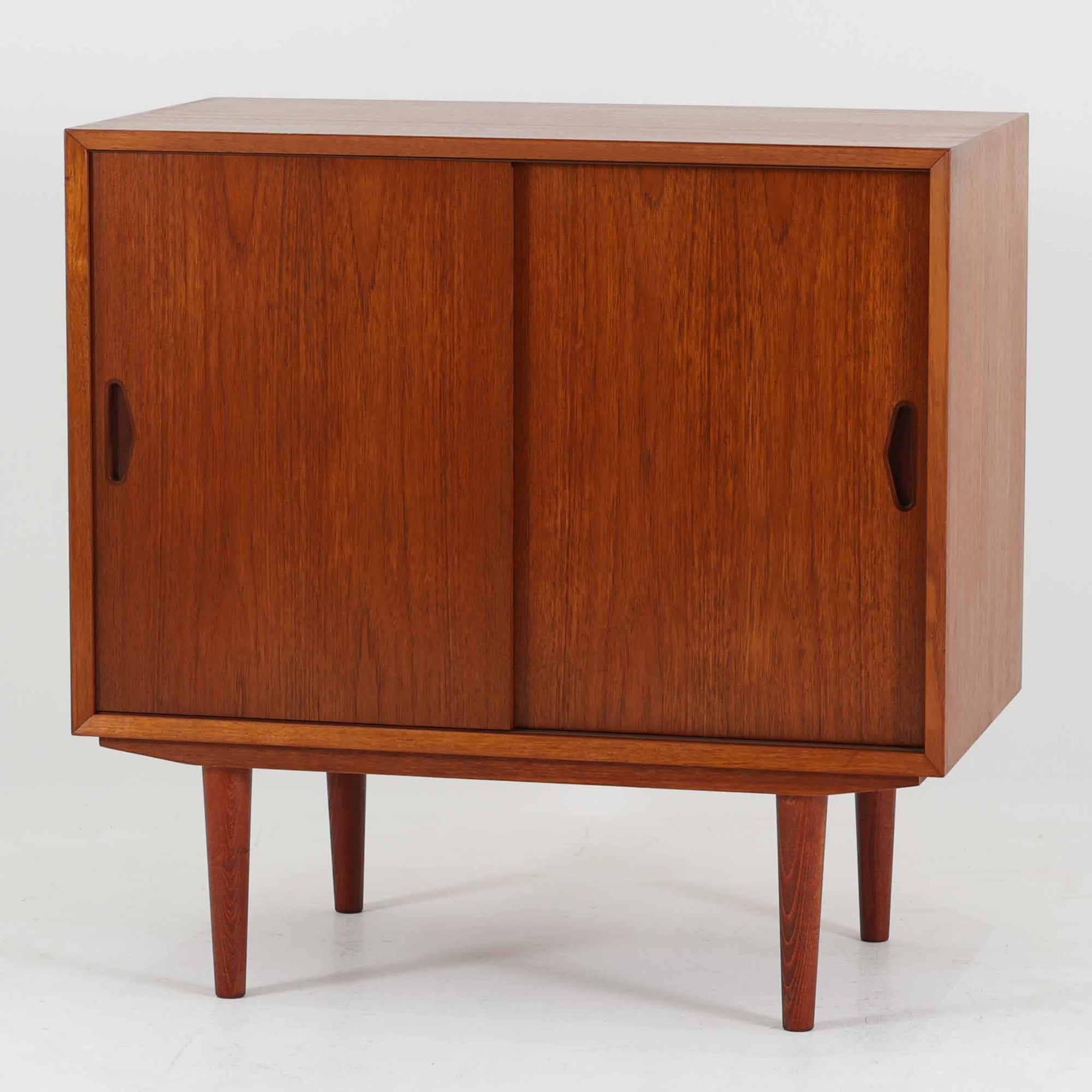 Olholm Mobelfabrik（オルホルム・モベルファブリック）によるデンマーク製のチーク材ボードです。幅80cmの取り入れやすいサイズに、すっきりとした引き戸と先細りの脚部を合わせた軽やかな佇まいが北欧らしい一台。内部は左右に棚板を備えた実用的な収納構造で、書籍や日用品、小物を整理しながら美しく収められます。経年により深みを増したチークの艶やかな木肌と、無駄を削ぎ落とした端正なフォルムが、リビングのサイドボードやベッドサイド収納として上質な存在感を演出。限られた空間にも置きやすく、ビンテージならではの丁寧な造りと希少性を楽しめる収納家具です。