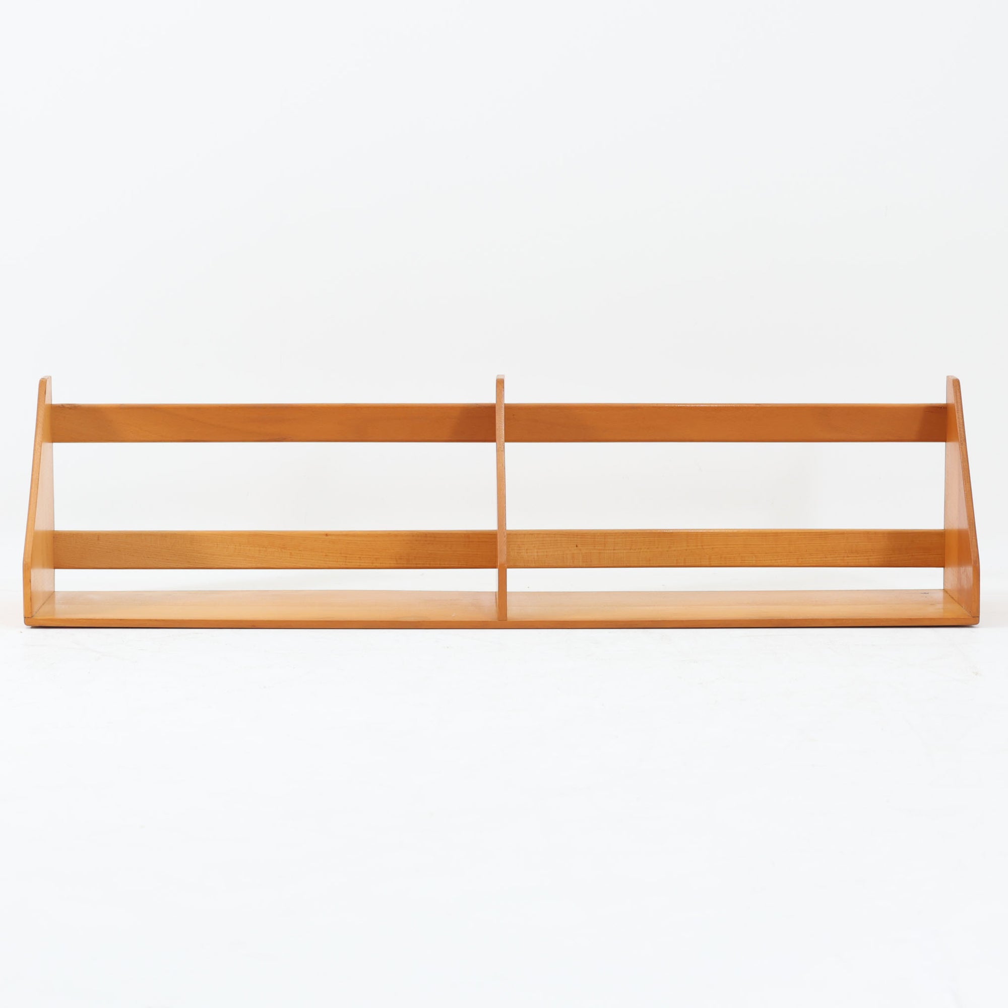 Borge Mogensen（ボーエ・モーエンセン）デザイン、FDB Mobler製のウォールシェルフ Model B5です。ビーチ無垢材を使用したシンプルで温かみのあるデザインが特徴で、北欧家具ならではの機能性と美しさを兼ね備えています。両サイドのパネルと背面のバー構造により、収納物が安定しやすく、実用性の高い設計となっています。中央の仕切りによって本や小物を整理しやすく、キッチンやリビング、書斎などさまざまな空間で活躍します。素朴で飽きのこないフォルムは、モーエンセンの「日常生活のための家具」という思想を体現したデザイン。デンマーク製の北欧ビンテージならではの味わい深い木の質感が魅力の一品です。