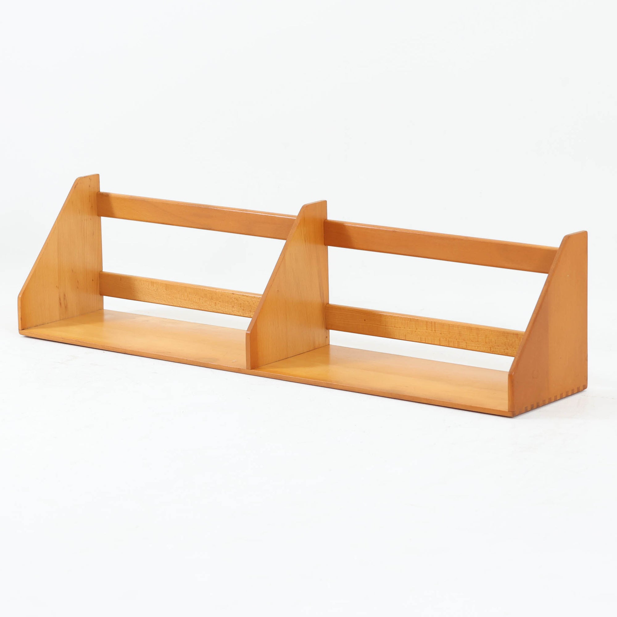 Borge Mogensen（ボーエ・モーエンセン）デザイン、FDB Mobler製のウォールシェルフ Model B5です。ビーチ無垢材を使用したシンプルで温かみのあるデザインが特徴で、北欧家具ならではの機能性と美しさを兼ね備えています。両サイドのパネルと背面のバー構造により、収納物が安定しやすく、実用性の高い設計となっています。中央の仕切りによって本や小物を整理しやすく、キッチンやリビング、書斎などさまざまな空間で活躍します。素朴で飽きのこないフォルムは、モーエンセンの「日常生活のための家具」という思想を体現したデザイン。デンマーク製の北欧ビンテージならではの味わい深い木の質感が魅力の一品です。