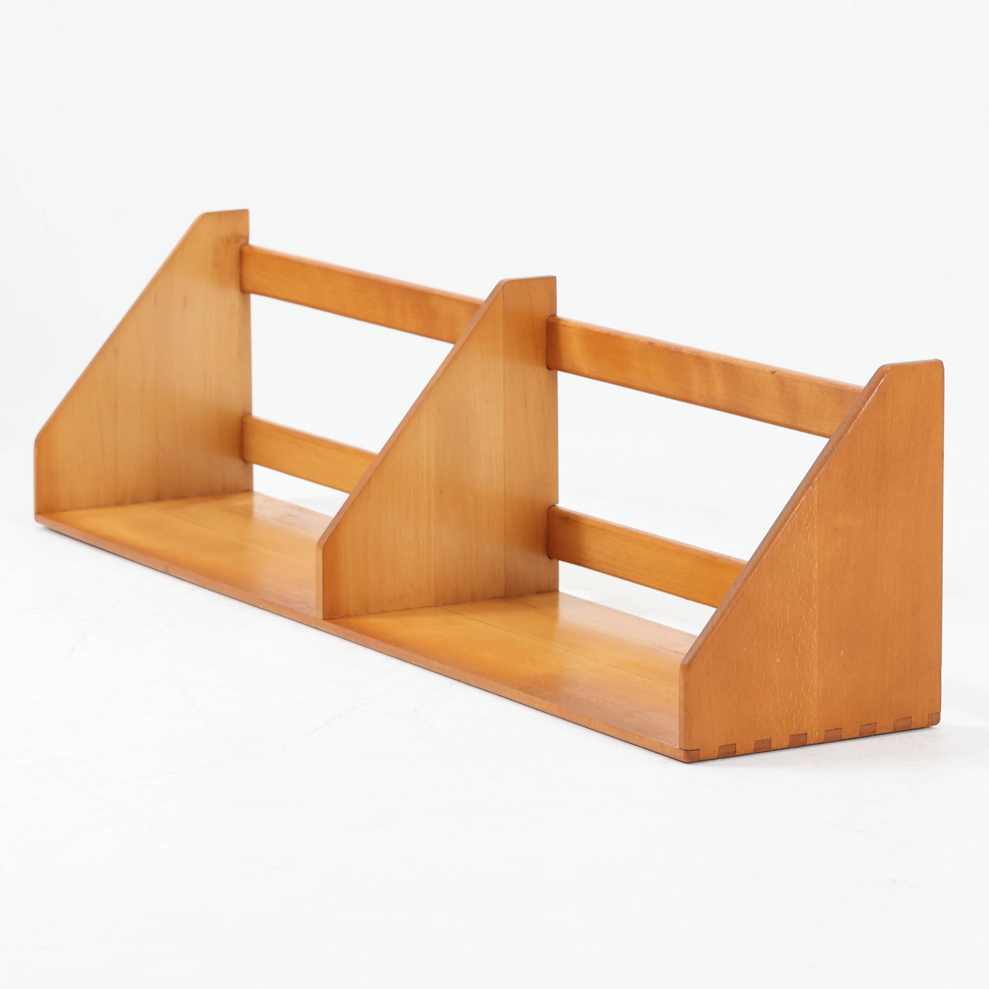 Borge Mogensen（ボーエ・モーエンセン）デザイン、FDB Mobler製のウォールシェルフ Model B5です。ビーチ無垢材を使用したシンプルで温かみのあるデザインが特徴で、北欧家具ならではの機能性と美しさを兼ね備えています。両サイドのパネルと背面のバー構造により、収納物が安定しやすく、実用性の高い設計となっています。中央の仕切りによって本や小物を整理しやすく、キッチンやリビング、書斎などさまざまな空間で活躍します。素朴で飽きのこないフォルムは、モーエンセンの「日常生活のための家具」という思想を体現したデザイン。デンマーク製の北欧ビンテージならではの味わい深い木の質感が魅力の一品です。