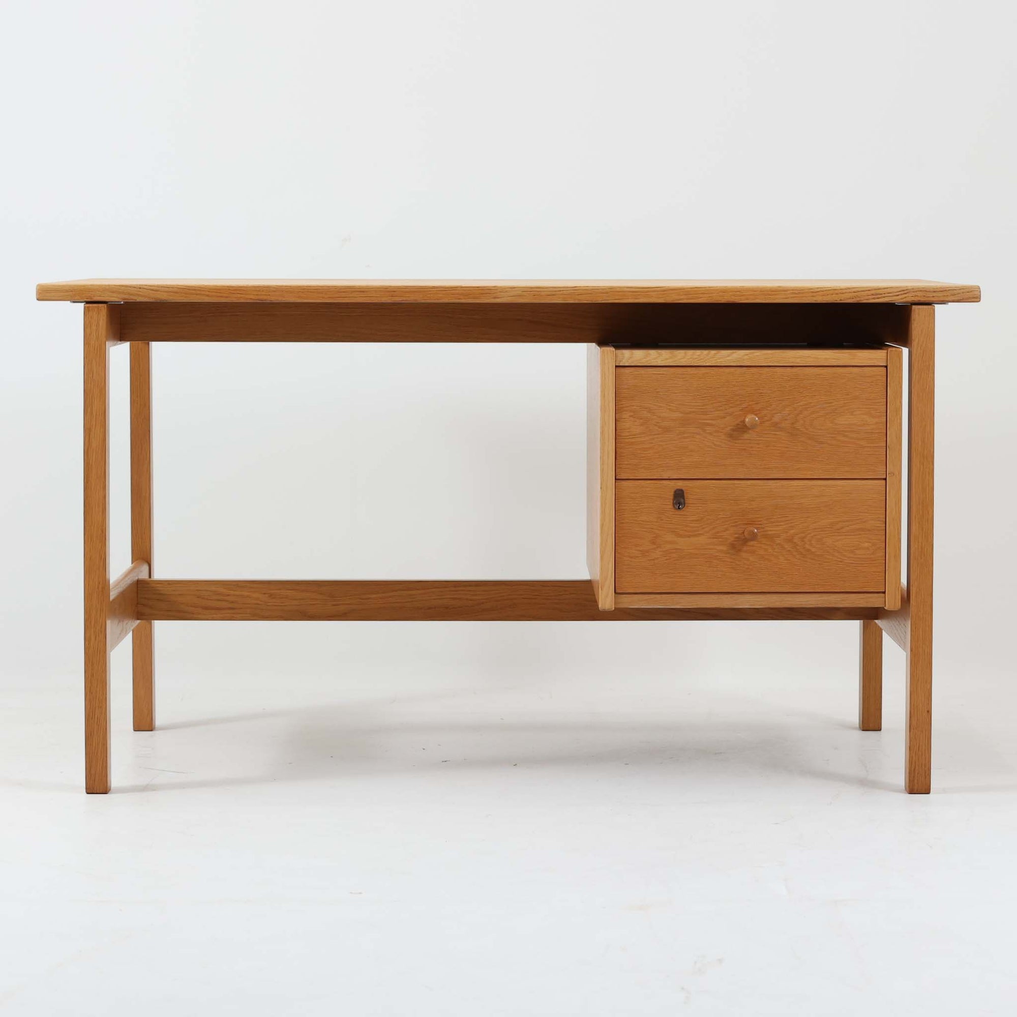 Hans J. Wegner（ハンス・J・ウェグナー）デザイン、Getama（ゲタマ）製GE156のオーク材片袖デスクです。幅125cmのゆとりある天板に、右側へ浮かぶように設けられた2段の片袖収納を組み合わせた、ウェグナーらしい端正な構造美が際立つ一台。無垢感のあるオークの木肌と軽快なフレーム構成が空間に明るく上質な印象をもたらし、書斎やホームオフィスはもちろん、ショップのワークテーブルとしても美しく映えます。引き出しは書類や文具を整理しやすく、下段には鍵付きで実用性も良好。名作椅子とも調和する洗練された佇まいと、北欧ビンテージならではの希少性が魅力のデスクです。