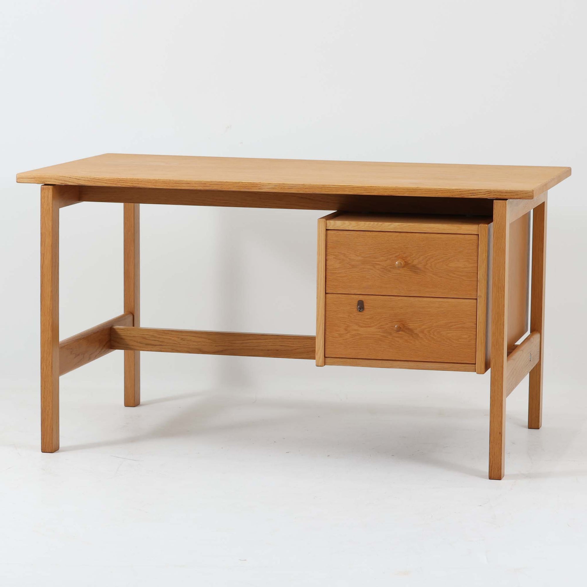 Hans J. Wegner（ハンス・J・ウェグナー）デザイン、Getama（ゲタマ）製GE156のオーク材片袖デスクです。幅125cmのゆとりある天板に、右側へ浮かぶように設けられた2段の片袖収納を組み合わせた、ウェグナーらしい端正な構造美が際立つ一台。無垢感のあるオークの木肌と軽快なフレーム構成が空間に明るく上質な印象をもたらし、書斎やホームオフィスはもちろん、ショップのワークテーブルとしても美しく映えます。引き出しは書類や文具を整理しやすく、下段には鍵付きで実用性も良好。名作椅子とも調和する洗練された佇まいと、北欧ビンテージならではの希少性が魅力のデスクです。