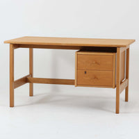 Hans J. Wegner（ハンス・J・ウェグナー）デザイン、Getama（ゲタマ）製GE156のオーク材片袖デスクです。幅125cmのゆとりある天板に、右側へ浮かぶように設けられた2段の片袖収納を組み合わせた、ウェグナーらしい端正な構造美が際立つ一台。無垢感のあるオークの木肌と軽快なフレーム構成が空間に明るく上質な印象をもたらし、書斎やホームオフィスはもちろん、ショップのワークテーブルとしても美しく映えます。引き出しは書類や文具を整理しやすく、下段には鍵付きで実用性も良好。名作椅子とも調和する洗練された佇まいと、北欧ビンテージならではの希少性が魅力のデスクです。