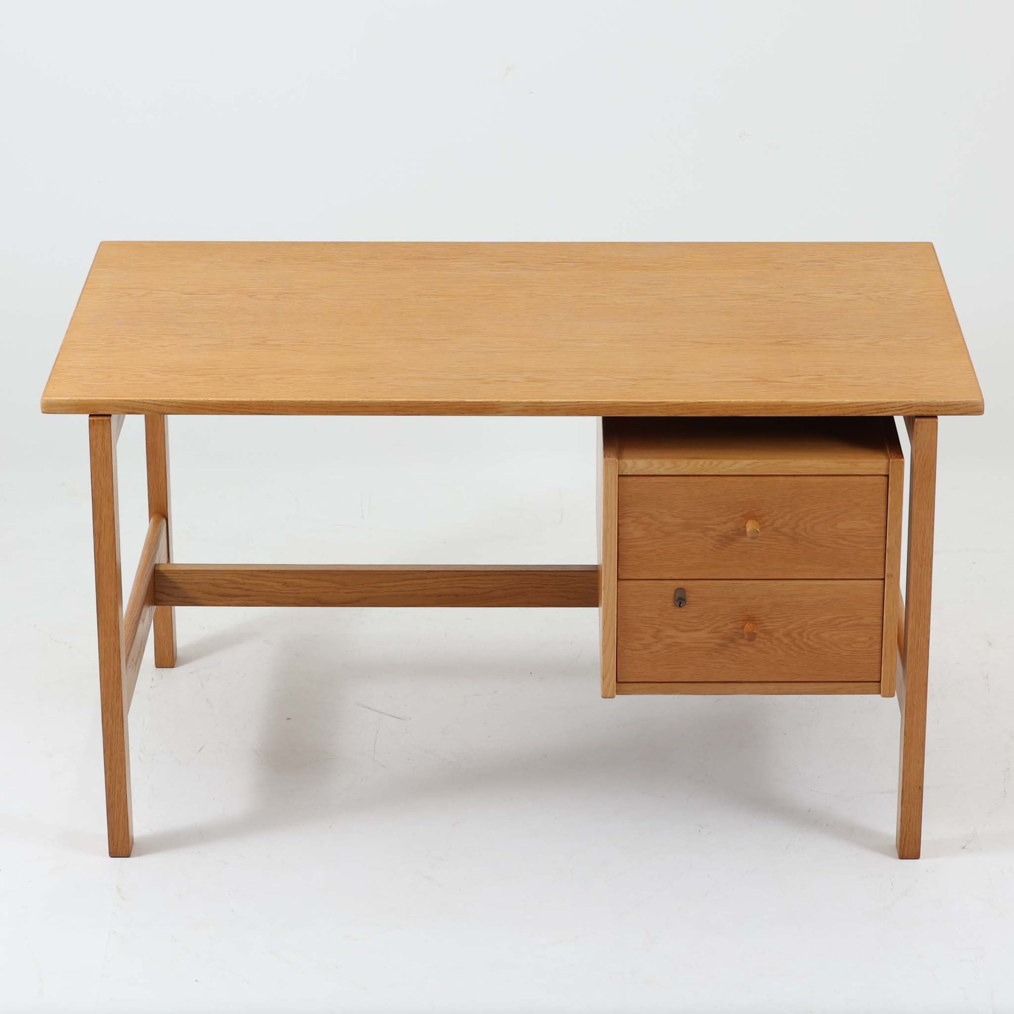 Hans J. Wegner（ハンス・J・ウェグナー）デザイン、Getama（ゲタマ）製GE156のオーク材片袖デスクです。幅125cmのゆとりある天板に、右側へ浮かぶように設けられた2段の片袖収納を組み合わせた、ウェグナーらしい端正な構造美が際立つ一台。無垢感のあるオークの木肌と軽快なフレーム構成が空間に明るく上質な印象をもたらし、書斎やホームオフィスはもちろん、ショップのワークテーブルとしても美しく映えます。引き出しは書類や文具を整理しやすく、下段には鍵付きで実用性も良好。名作椅子とも調和する洗練された佇まいと、北欧ビンテージならではの希少性が魅力のデスクです。