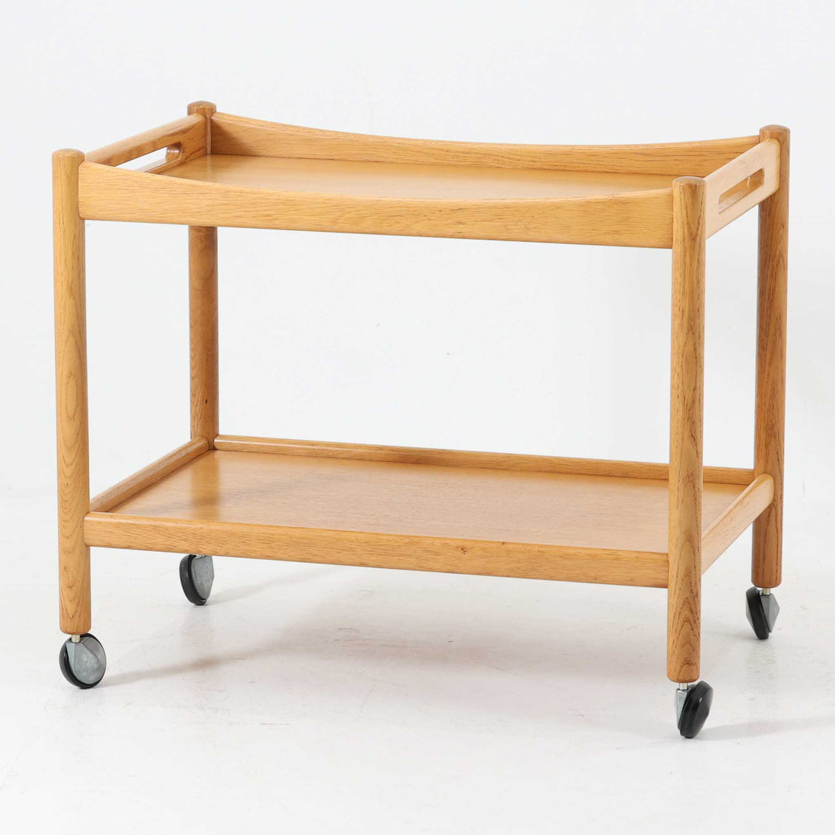 Hans J. Wegnerがデザインし、PP Moblerが製造したAT45のキャスターワゴンです。明るく温かなオーク材を用い、上下2段の棚板と四隅のキャスターを組み合わせた、移動性に優れた実用的な構成が特徴。上段には持ち手を兼ねる開口部が設けられ、緩やかに湾曲する側板や丸みのある支柱など、ウェグナーらしい柔らかな造形と丁寧な木工技術が感じられます。経年によって深まった木肌を楽しみながら、キッチンやダイニング、リビングで配膳や収納に活躍する一台です。