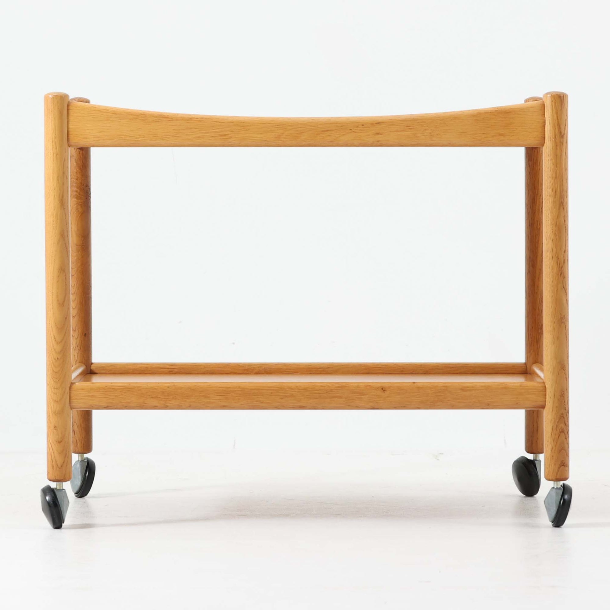 Hans J. Wegnerがデザインし、PP Moblerが製造したAT45のキャスターワゴンです。明るく温かなオーク材を用い、上下2段の棚板と四隅のキャスターを組み合わせた、移動性に優れた実用的な構成が特徴。上段には持ち手を兼ねる開口部が設けられ、緩やかに湾曲する側板や丸みのある支柱など、ウェグナーらしい柔らかな造形と丁寧な木工技術が感じられます。経年によって深まった木肌を楽しみながら、キッチンやダイニング、リビングで配膳や収納に活躍する一台です。