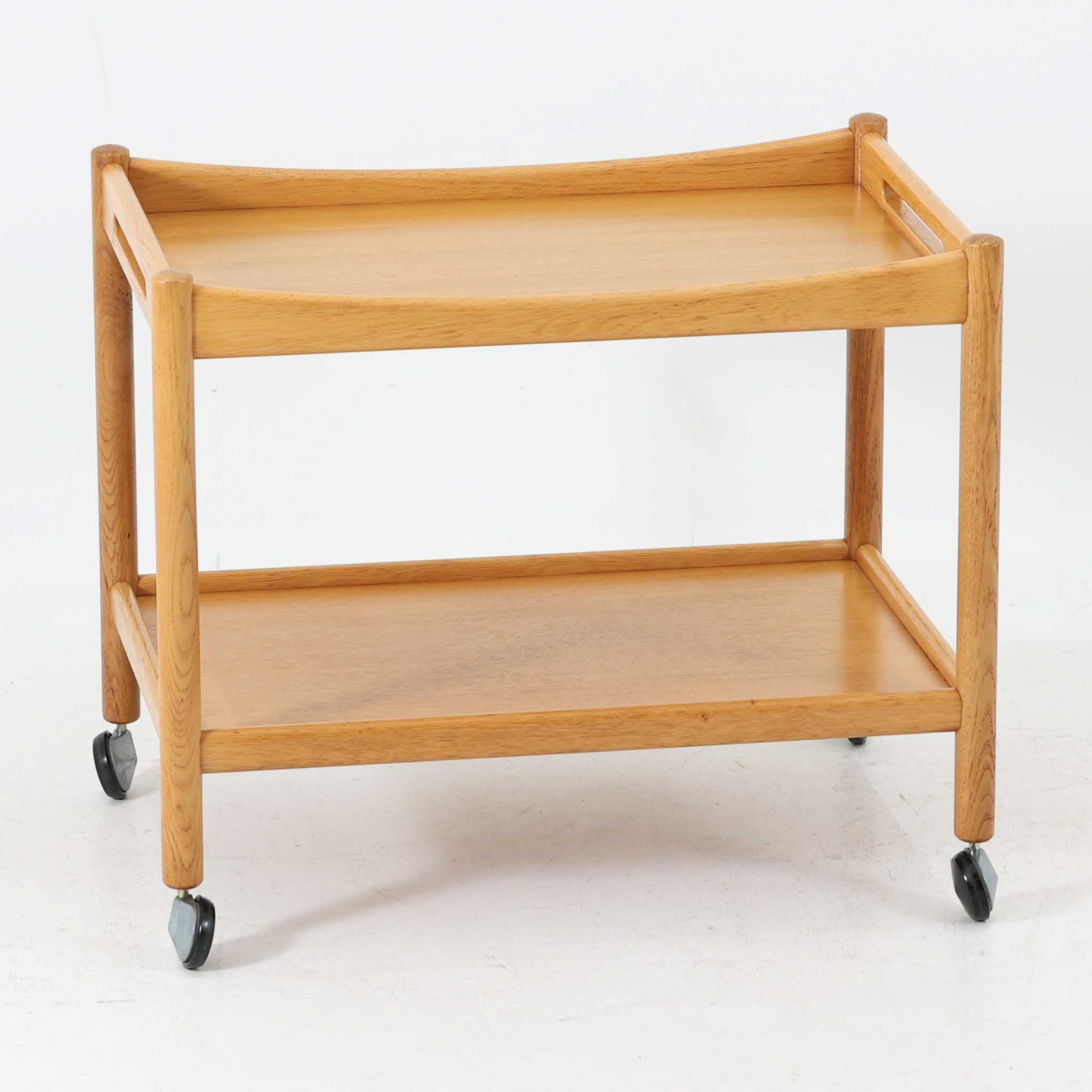 Hans J. Wegnerがデザインし、PP Moblerが製造したAT45のキャスターワゴンです。明るく温かなオーク材を用い、上下2段の棚板と四隅のキャスターを組み合わせた、移動性に優れた実用的な構成が特徴。上段には持ち手を兼ねる開口部が設けられ、緩やかに湾曲する側板や丸みのある支柱など、ウェグナーらしい柔らかな造形と丁寧な木工技術が感じられます。経年によって深まった木肌を楽しみながら、キッチンやダイニング、リビングで配膳や収納に活躍する一台です。