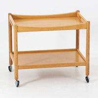 Hans J. Wegnerがデザインし、PP Moblerが製造したAT45のキャスターワゴンです。明るく温かなオーク材を用い、上下2段の棚板と四隅のキャスターを組み合わせた、移動性に優れた実用的な構成が特徴。上段には持ち手を兼ねる開口部が設けられ、緩やかに湾曲する側板や丸みのある支柱など、ウェグナーらしい柔らかな造形と丁寧な木工技術が感じられます。経年によって深まった木肌を楽しみながら、キッチンやダイニング、リビングで配膳や収納に活躍する一台です。