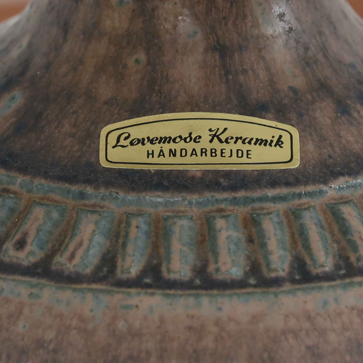 デンマークのLovemose Keramikによる陶磁器製のテーブルランプ。ふっくらと丸みを帯びたボディから細く伸びる首元へと続く、優美でバランスの取れたフォルムが印象的な一台です。ブラウンやグレーが複雑に混ざり合う釉薬には、流れるような濃淡や細かな斑点模様が現れ、陶磁器ならではの豊かな表情を楽しめます。首元と胴体の境目には連続した彫り模様が施され、素朴な風合いの中に職人の丁寧な手仕事が感じられます。シンプルなリネンシェードを組み合わせることで、点灯時には柔らかな光が広がり、落ち着いた空間を演出します。リビングのサイドボードや寝室のベッドサイドなどにおすすめの、北欧ビンテージらしい温もりと存在感を備えた照明です。