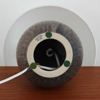 デンマークのLovemose Keramikによる陶磁器製のテーブルランプ。ふっくらと丸みを帯びたボディから細く伸びる首元へと続く、優美でバランスの取れたフォルムが印象的な一台です。ブラウンやグレーが複雑に混ざり合う釉薬には、流れるような濃淡や細かな斑点模様が現れ、陶磁器ならではの豊かな表情を楽しめます。首元と胴体の境目には連続した彫り模様が施され、素朴な風合いの中に職人の丁寧な手仕事が感じられます。シンプルなリネンシェードを組み合わせることで、点灯時には柔らかな光が広がり、落ち着いた空間を演出します。リビングのサイドボードや寝室のベッドサイドなどにおすすめの、北欧ビンテージらしい温もりと存在感を備えた照明です。