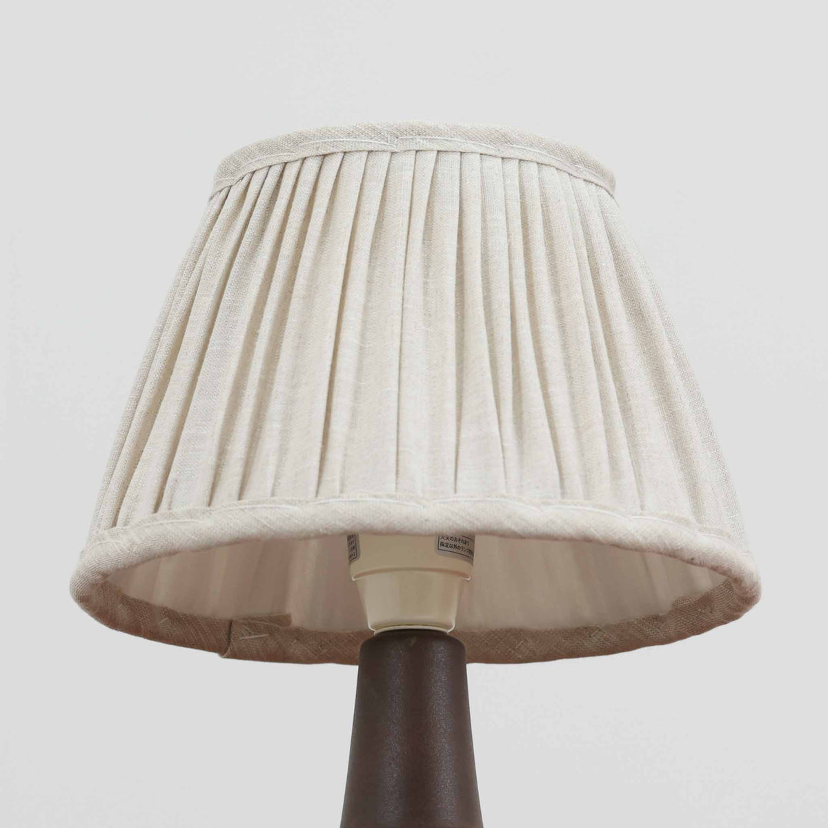 デンマークの陶磁器メーカーSoholm Keramik（スーホルム）による、Einar Johansen（アイナー・ヨハンセン）デザインのビンテージテーブルランプ。すっきりと伸びた首元から裾に向かって広がる陶磁器製ベースは、落ち着いたブラウンと鮮やかなブルーの釉薬が織りなす美しい色彩が特徴です。胴部には連続する幾何学模様のレリーフが施され、釉薬の濃淡と立体的な陰影が豊かな表情を生み出しています。素朴な陶器の質感と、繊細なプリーツを施した白いリネンシェードの組み合わせも魅力的。点灯すると布越しに柔らかな光が広がり、空間を温かく包み込みます。北欧らしい造形美とクラフトマンシップが感じられる一台で、リビングや寝室のアクセント照明としておすすめです。