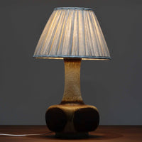 デンマークの陶磁器メーカーAxella Keramik（アクセラ）による、Jette Helleroe（イェッテ・ヘレロー）デザインのビンテージテーブルランプ。すらりと伸びた細身の首元と、ふっくらと丸みを帯びたベースが印象的な、美しいシルエットの一台です。陶磁器製の本体には、アイボリーを基調とした柔らかな色合いに、深みのあるブラウンの釉薬が大胆に施され、流れるような色の境界や自然な濃淡が豊かな表情を生み出しています。釉薬の重なりによって生まれる独特の風合いには、手仕事ならではの温もりと芸術性が感じられます。プリーツを施したリネンシェードは柔らかな光を広げ、存在感のあるベースとの美しい調和を演出します。リビングのサイドボードや寝室など、空間を印象的に彩るアクセント照明としておすすめです。