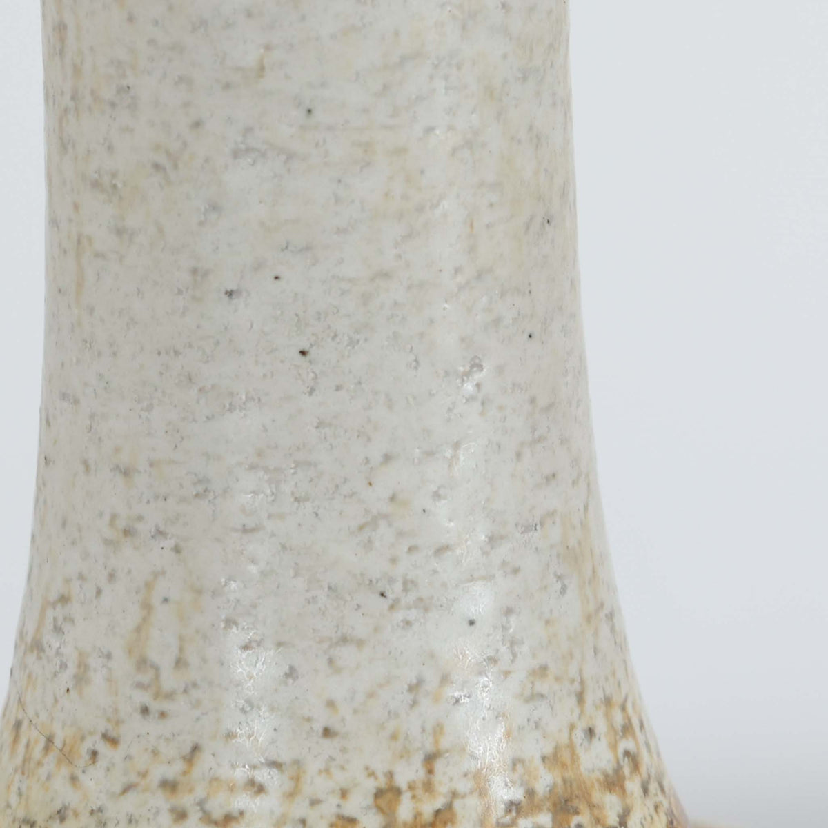 デンマークの陶磁器メーカーAxella Keramik（アクセラ）による、Jette Helleroe（イェッテ・ヘレロー）デザインのビンテージテーブルランプ。すらりと伸びた細身の首元と、ふっくらと丸みを帯びたベースが印象的な、美しいシルエットの一台です。陶磁器製の本体には、アイボリーを基調とした柔らかな色合いに、深みのあるブラウンの釉薬が大胆に施され、流れるような色の境界や自然な濃淡が豊かな表情を生み出しています。釉薬の重なりによって生まれる独特の風合いには、手仕事ならではの温もりと芸術性が感じられます。プリーツを施したリネンシェードは柔らかな光を広げ、存在感のあるベースとの美しい調和を演出します。リビングのサイドボードや寝室など、空間を印象的に彩るアクセント照明としておすすめです。