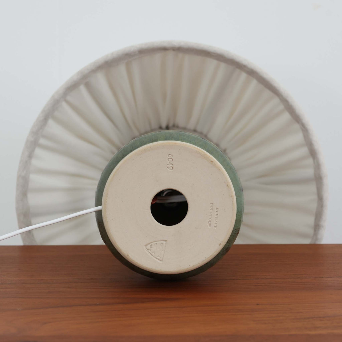 デンマークの陶磁器メーカーMichael Andersen &amp; Son（ミケル・アナセン＆サン）によるビンテージテーブルランプ。すらりと伸びた円錐形のフォルムと、裾に向かってふっくらと広がる優美なシルエットが印象的な一台です。深みのあるグリーンを基調とした釉薬には、自然な濃淡や繊細な色の変化が見られ、陶磁器ならではの豊かな風合いを楽しめます。ベース下部には菱形のレリーフ模様が連続して施され、立体的な陰影がデザインに美しいアクセントを添えています。プリーツを施したリネンシェードからは柔らかな光が広がり、落ち着いた温もりのある空間を演出します。北欧ビンテージらしい素朴さと洗練された造形美を兼ね備え、リビングのサイドボードや寝室のベッドサイドなどにおすすめです。