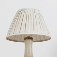 デンマークの陶磁器メーカーAxella Keramik（アクセラ）による、Jette Helleroe（イェッテ・ヘレロー）デザインのビンテージテーブルランプ。丸みを帯びたふっくらとしたベースから、細く伸びる首元へとつながる彫刻的なフォルムが印象的な一品です。温かみのあるアイボリーを基調に、深いブラウンの釉薬を大胆に配した独特の模様が特徴で、釉薬の自然な濃淡や境界のにじみが、手仕事ならではの豊かな表情を生み出しています。素朴さと芸術性を兼ね備えた佇まいは、北欧ビンテージならではの魅力を感じさせます。プリーツを施したリネンシェードは柔らかな光を広げ、落ち着いた温もりのある空間を演出します。リビングのサイドボードや寝室のチェストなどに置けば、消灯時にもオブジェのような存在感を楽しめます。