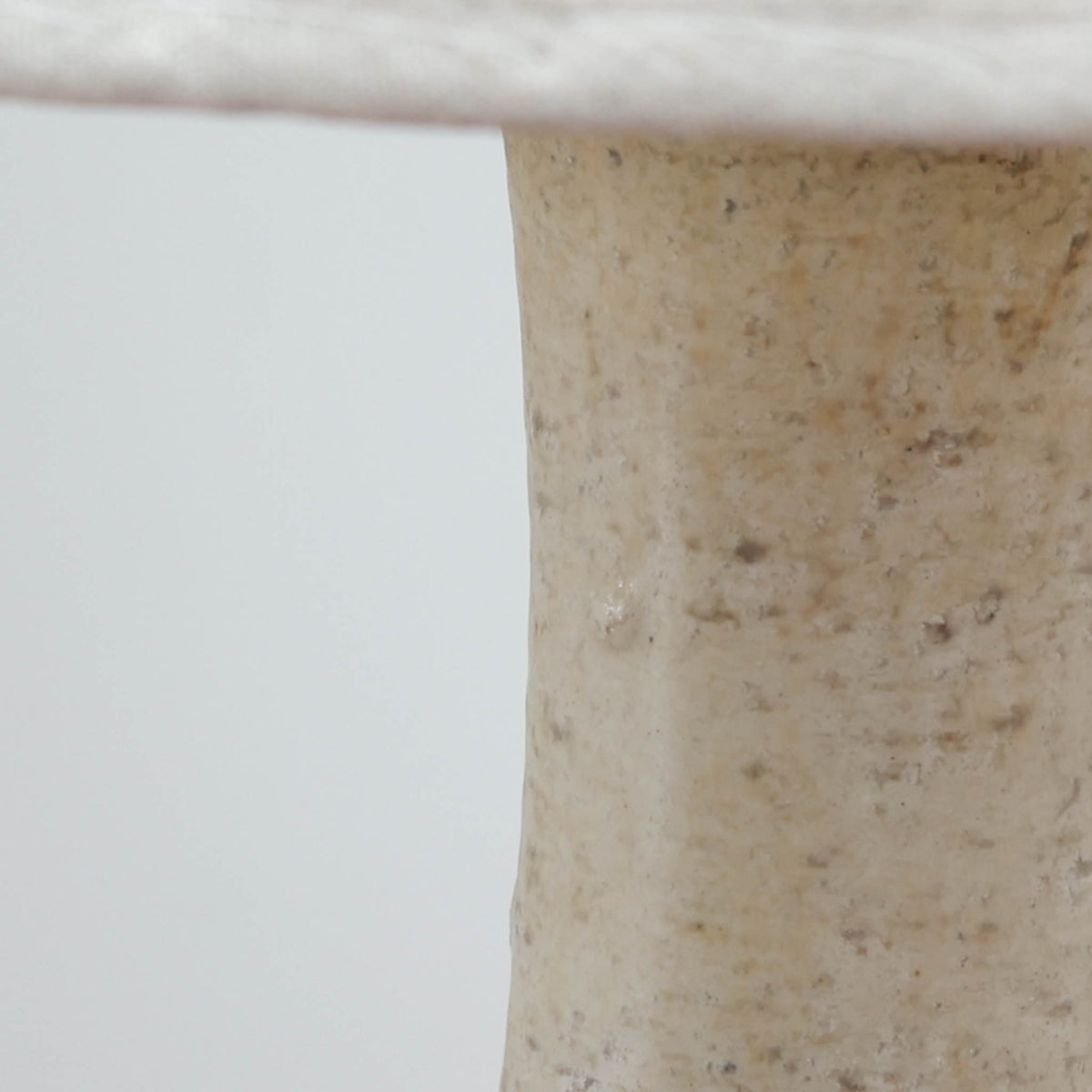 デンマークの陶磁器メーカーAxella Keramik（アクセラ）による、Jette Helleroe（イェッテ・ヘレロー）デザインのビンテージテーブルランプ。丸みを帯びたふっくらとしたベースから、細く伸びる首元へとつながる彫刻的なフォルムが印象的な一品です。温かみのあるアイボリーを基調に、深いブラウンの釉薬を大胆に配した独特の模様が特徴で、釉薬の自然な濃淡や境界のにじみが、手仕事ならではの豊かな表情を生み出しています。素朴さと芸術性を兼ね備えた佇まいは、北欧ビンテージならではの魅力を感じさせます。プリーツを施したリネンシェードは柔らかな光を広げ、落ち着いた温もりのある空間を演出します。リビングのサイドボードや寝室のチェストなどに置けば、消灯時にもオブジェのような存在感を楽しめます。