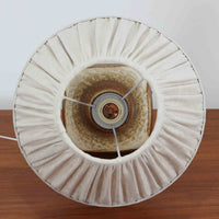 デンマークの陶磁器メーカーAxella Keramik（アクセラ）による、Jette Helleroe（イェッテ・ヘレロー）デザインのビンテージテーブルランプ。丸みを帯びたふっくらとしたベースから、細く伸びる首元へとつながる彫刻的なフォルムが印象的な一品です。温かみのあるアイボリーを基調に、深いブラウンの釉薬を大胆に配した独特の模様が特徴で、釉薬の自然な濃淡や境界のにじみが、手仕事ならではの豊かな表情を生み出しています。素朴さと芸術性を兼ね備えた佇まいは、北欧ビンテージならではの魅力を感じさせます。プリーツを施したリネンシェードは柔らかな光を広げ、落ち着いた温もりのある空間を演出します。リビングのサイドボードや寝室のチェストなどに置けば、消灯時にもオブジェのような存在感を楽しめます。