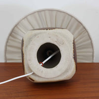 デンマークの陶磁器メーカーAxella Keramik（アクセラ）による、Jette Helleroe（イェッテ・ヘレロー）デザインのビンテージテーブルランプ。丸みを帯びたふっくらとしたベースから、細く伸びる首元へとつながる彫刻的なフォルムが印象的な一品です。温かみのあるアイボリーを基調に、深いブラウンの釉薬を大胆に配した独特の模様が特徴で、釉薬の自然な濃淡や境界のにじみが、手仕事ならではの豊かな表情を生み出しています。素朴さと芸術性を兼ね備えた佇まいは、北欧ビンテージならではの魅力を感じさせます。プリーツを施したリネンシェードは柔らかな光を広げ、落ち着いた温もりのある空間を演出します。リビングのサイドボードや寝室のチェストなどに置けば、消灯時にもオブジェのような存在感を楽しめます。