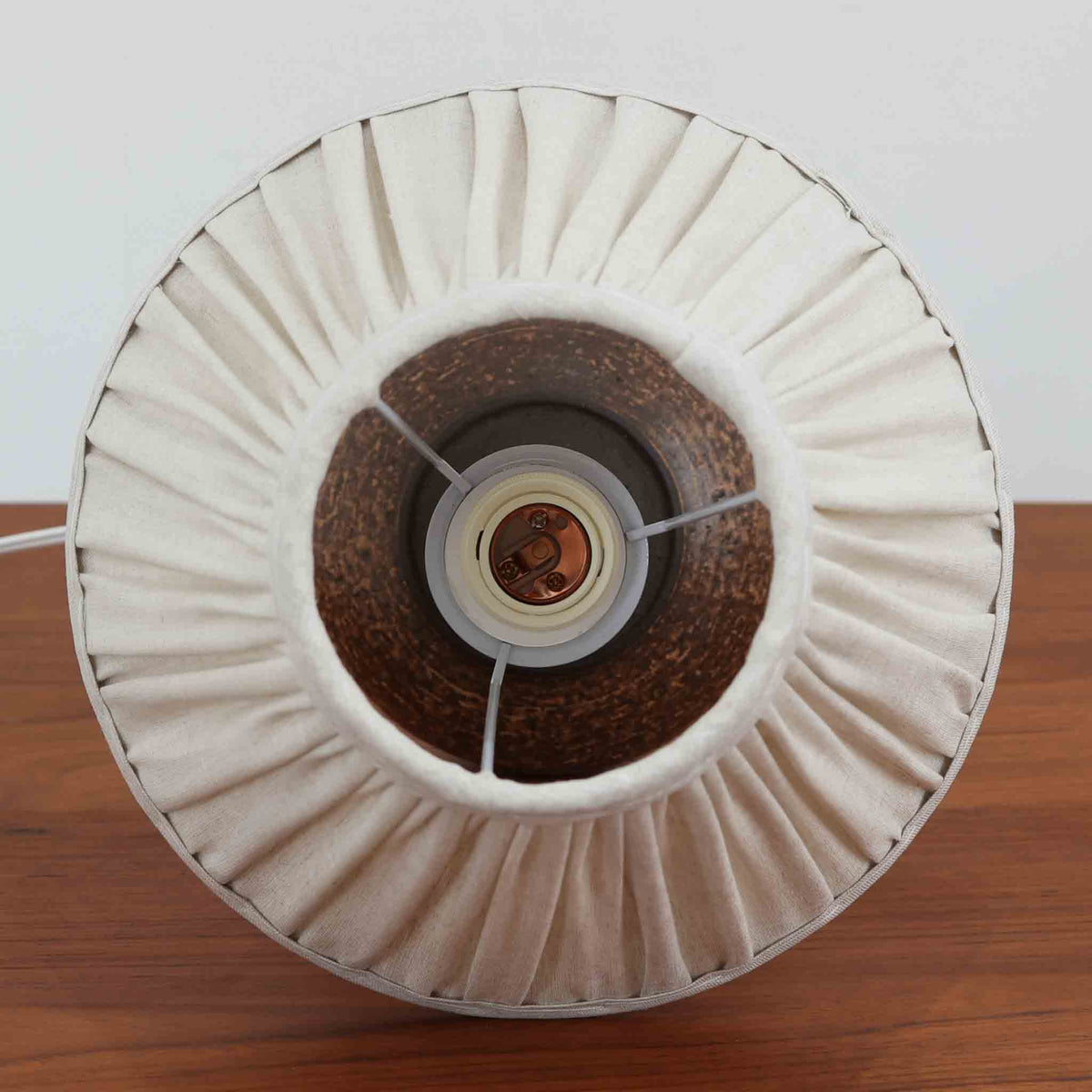 デンマーク製のビンテージテーブルランプ。陶磁器製のベースは、ふっくらと丸みを帯びた下部と、中央が緩やかにくびれた細長い首元を組み合わせた、彫刻的なフォルムが印象的です。深みのあるダークブラウンを基調に、下部には褐色の濃淡が複雑に重なり、ざらりとした質感や釉薬の表情が焼き物ならではの素朴な魅力を引き立てています。落ち着いた色合いながらも存在感があり、北欧ビンテージらしい温もりと力強さを感じさせる佇まいです。細かなプリーツを施したリネンシェードは、点灯すると柔らかな光を広げ、穏やかで心地よい雰囲気を演出します。リビングのサイドボードや寝室のベッドサイドなどにおすすめの一品です。