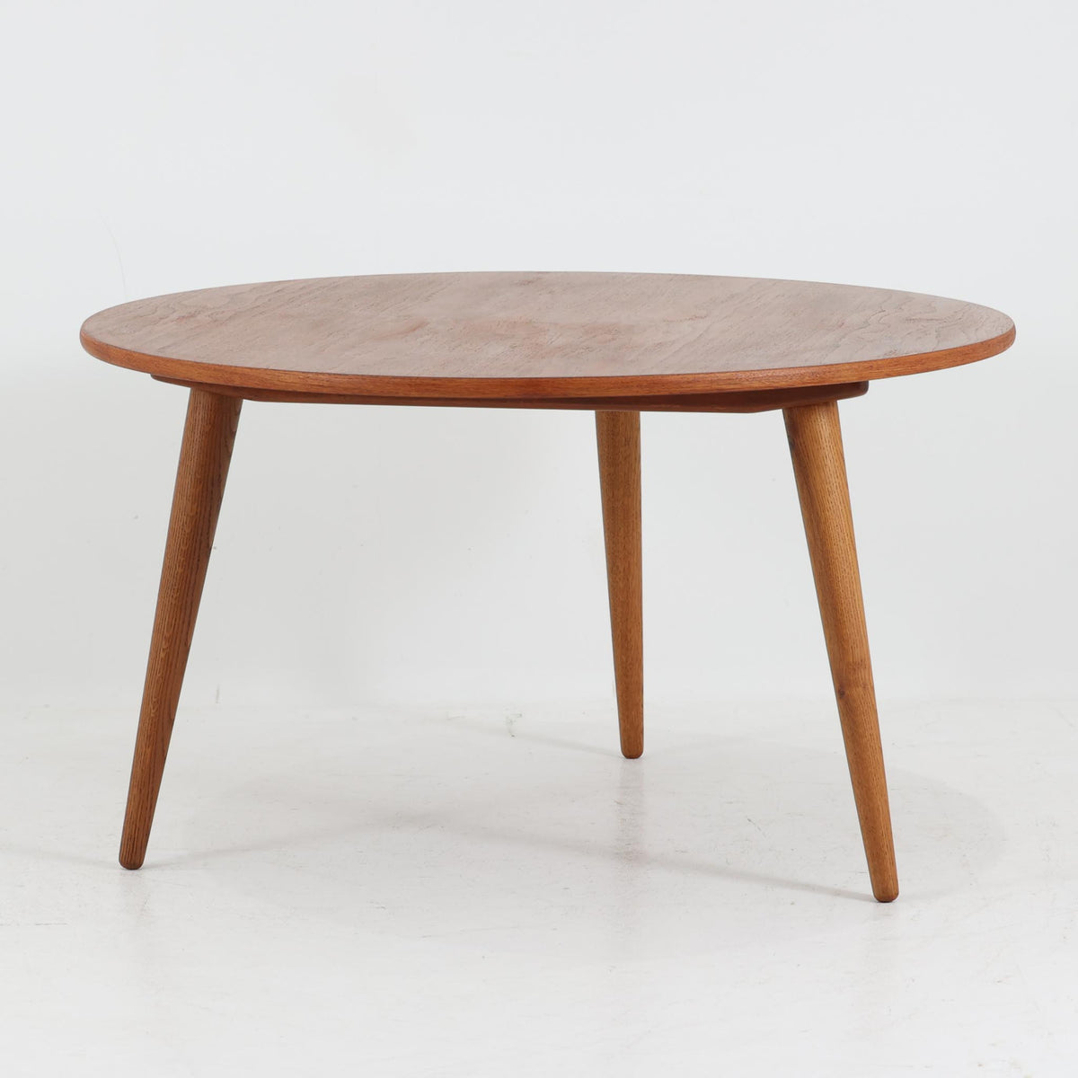 Hans J. Wegnerがデザインし、Andreas Tuckが製造を手掛けたAT8。チーク材の円形天板とオーク材の脚部を組み合わせ、異なる木材の表情を巧みに生かした一台です。直径98cmの伸びやかな天板を、外側へ緩やかに開く4本のテーパードレッグが軽快に支えるシンプルな構成で、素材とプロポーションの美しさが際立ちます。ソファを囲むリビングの主役として取り入れやすく、ウェグナーらしい端正な造形と年月を重ねた木部の風合いを味わえるビンテージ品です。
