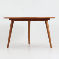 Hans J. Wegnerがデザインし、Andreas Tuckが製造を手掛けたAT8。チーク材の円形天板とオーク材の脚部を組み合わせ、異なる木材の表情を巧みに生かした一台です。直径98cmの伸びやかな天板を、外側へ緩やかに開く4本のテーパードレッグが軽快に支えるシンプルな構成で、素材とプロポーションの美しさが際立ちます。ソファを囲むリビングの主役として取り入れやすく、ウェグナーらしい端正な造形と年月を重ねた木部の風合いを味わえるビンテージ品です。