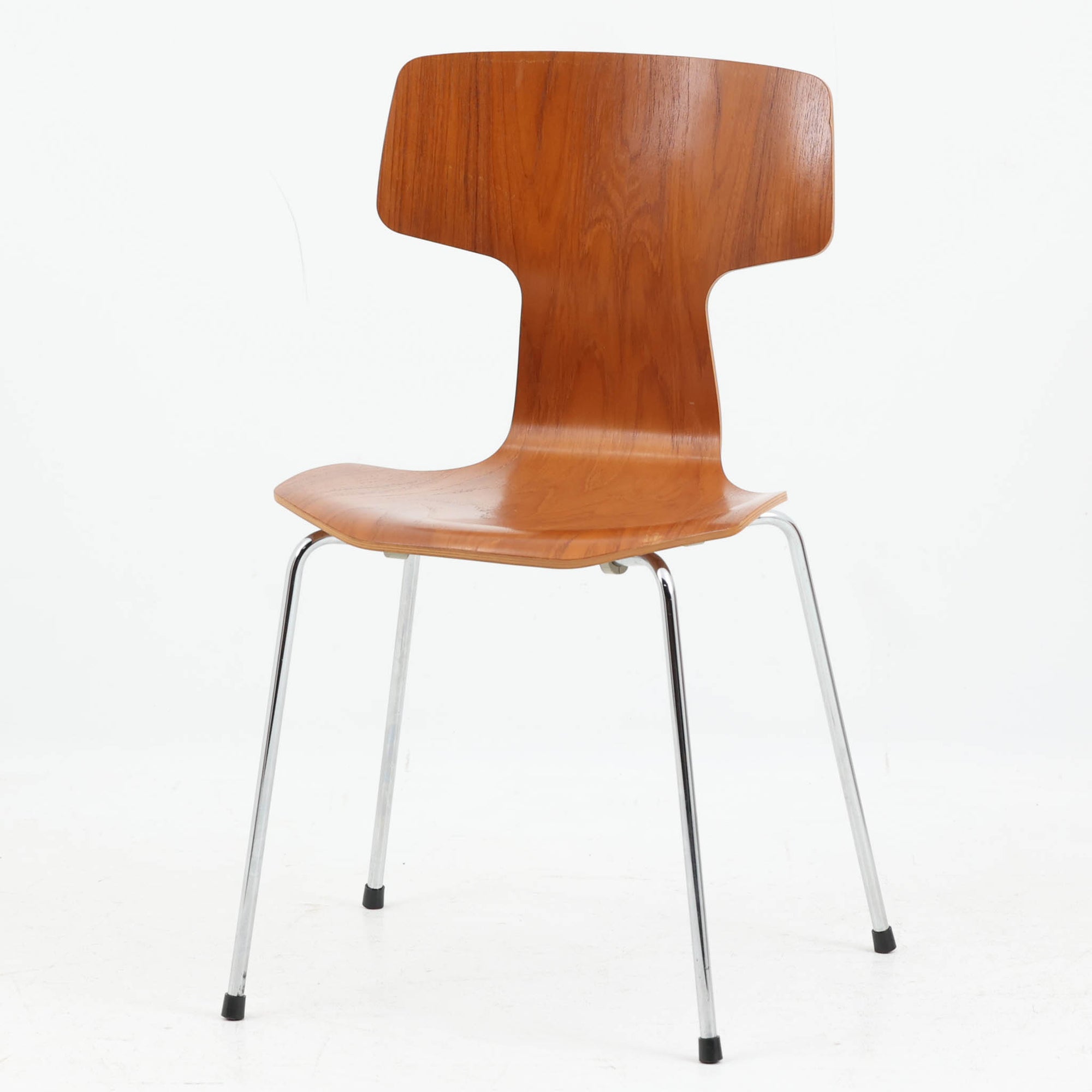 アルネ・ヤコブセンがデザインし、Fritz Hansenが製造した「T Chair」です。チーク材の成形合板による背座一体型のシェルは、背面上部を左右に広げた特徴的なシルエットと、身体に沿う緩やかな曲面が魅力。細身の金属脚との組み合わせが軽快で、ダイニングはもちろん、書斎や玄関のアクセントチェアにもおすすめです。美しい木目と時を重ねた風合い、合理的な構造に宿る北欧ビンテージらしい存在感を楽しめます。