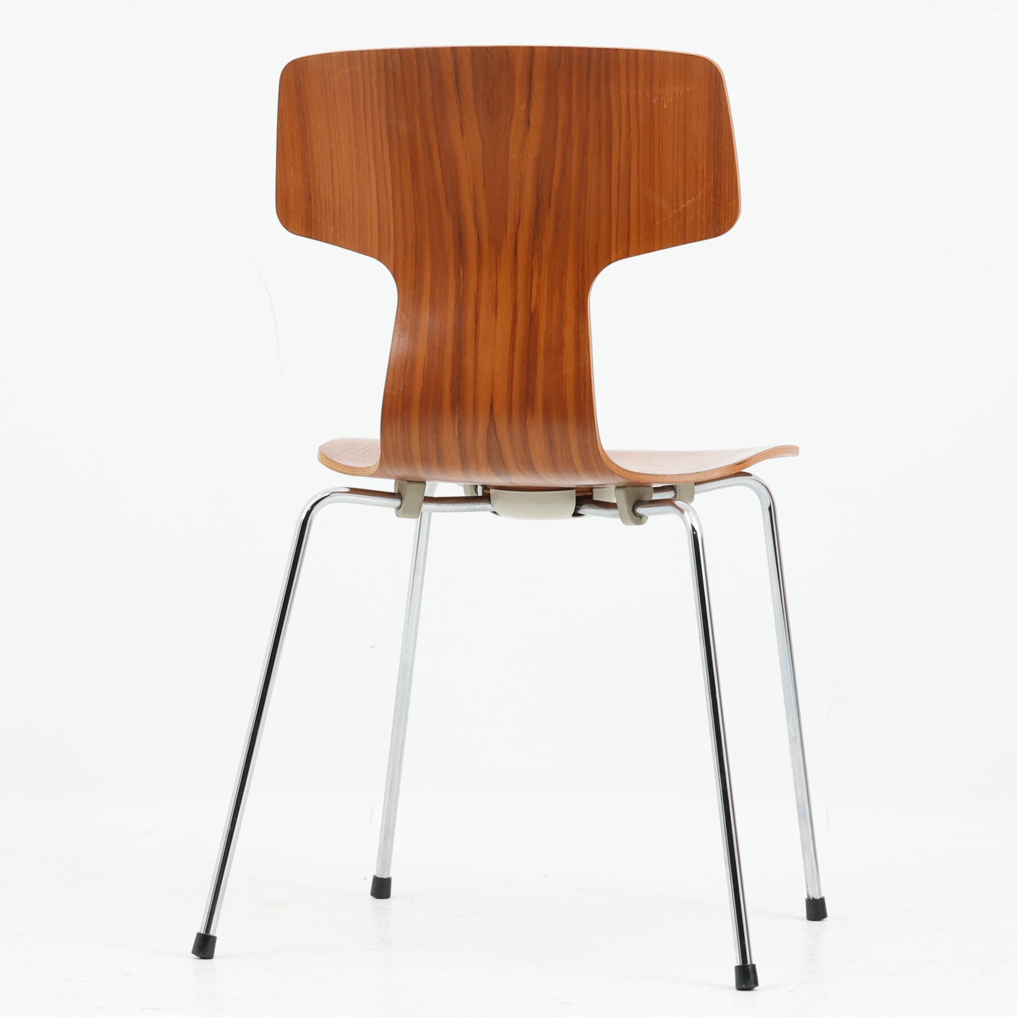 アルネ・ヤコブセンがデザインし、Fritz Hansenが製造した「T Chair」です。チーク材の成形合板による背座一体型のシェルは、背面上部を左右に広げた特徴的なシルエットと、身体に沿う緩やかな曲面が魅力。細身の金属脚との組み合わせが軽快で、ダイニングはもちろん、書斎や玄関のアクセントチェアにもおすすめです。美しい木目と時を重ねた風合い、合理的な構造に宿る北欧ビンテージらしい存在感を楽しめます。