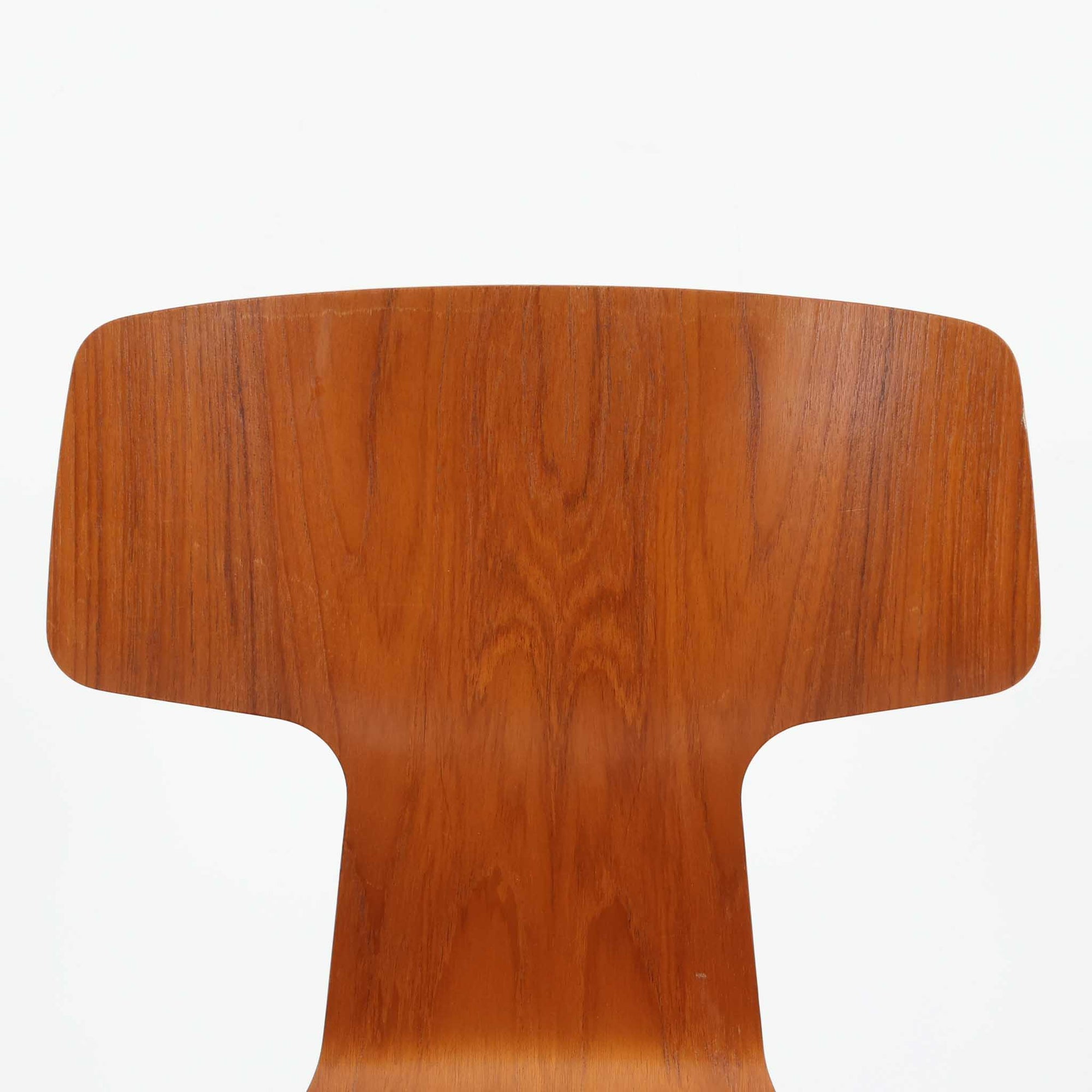 アルネ・ヤコブセンがデザインし、Fritz Hansenが製造した「T Chair」です。チーク材の成形合板による背座一体型のシェルは、背面上部を左右に広げた特徴的なシルエットと、身体に沿う緩やかな曲面が魅力。細身の金属脚との組み合わせが軽快で、ダイニングはもちろん、書斎や玄関のアクセントチェアにもおすすめです。美しい木目と時を重ねた風合い、合理的な構造に宿る北欧ビンテージらしい存在感を楽しめます。