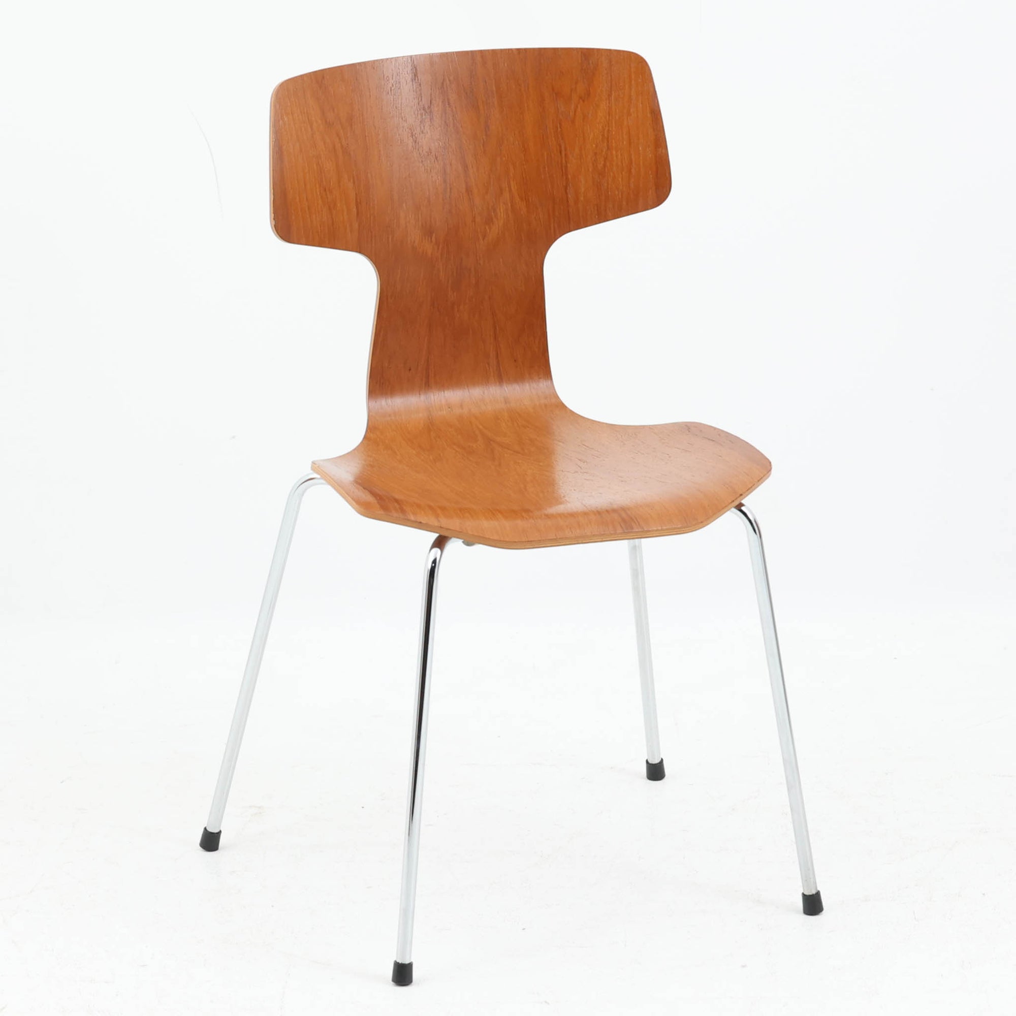 アルネ・ヤコブセンがデザインし、Fritz Hansenが製造した「T Chair」です。チーク材の成形合板による背座一体型のシェルは、背面上部を左右に広げた特徴的なシルエットと、身体に沿う緩やかな曲面が魅力。細身の金属脚との組み合わせが軽快で、ダイニングはもちろん、書斎や玄関のアクセントチェアにもおすすめです。美しい木目と時を重ねた風合い、合理的な構造に宿る北欧ビンテージらしい存在感を楽しめます。