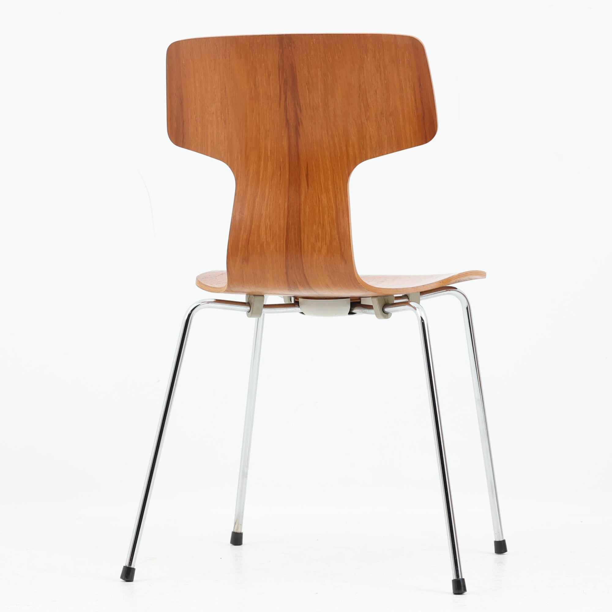 アルネ・ヤコブセンがデザインし、Fritz Hansenが製造した「T Chair」です。チーク材の成形合板による背座一体型のシェルは、背面上部を左右に広げた特徴的なシルエットと、身体に沿う緩やかな曲面が魅力。細身の金属脚との組み合わせが軽快で、ダイニングはもちろん、書斎や玄関のアクセントチェアにもおすすめです。美しい木目と時を重ねた風合い、合理的な構造に宿る北欧ビンテージらしい存在感を楽しめます。