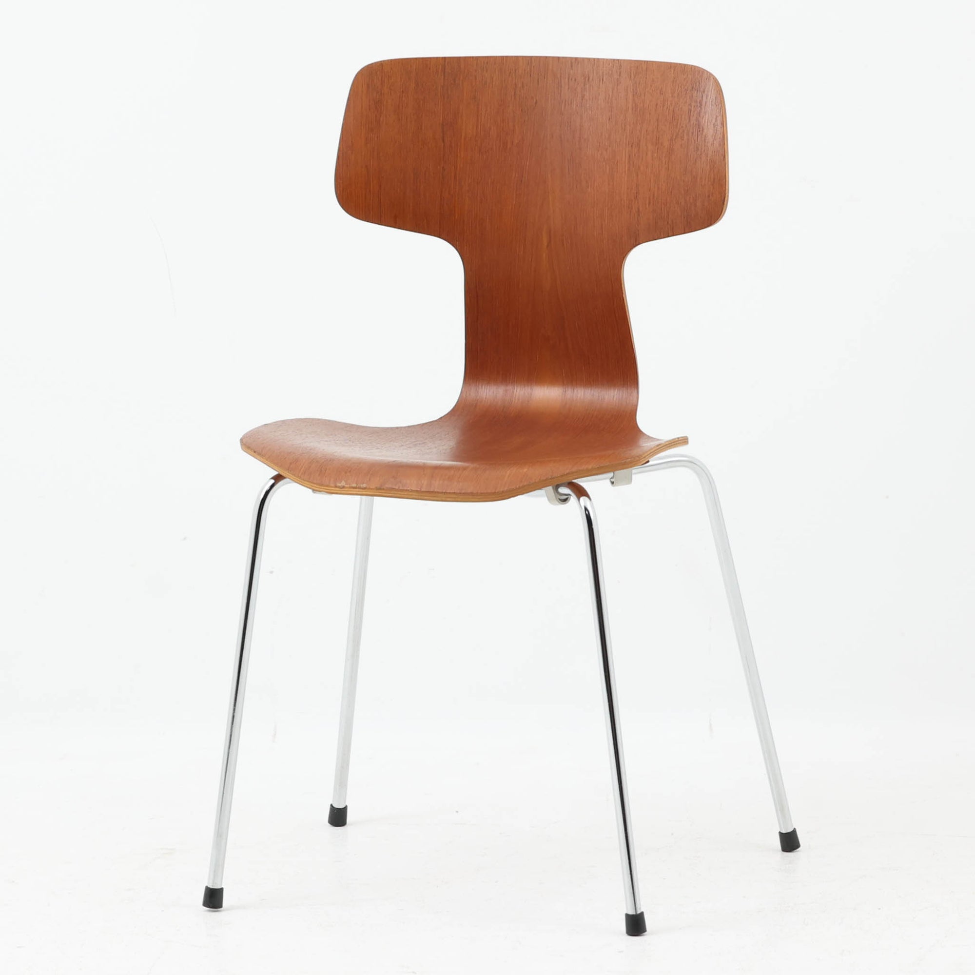 アルネ・ヤコブセンがデザインし、Fritz Hansenが製造した「T Chair」です。チーク材の成形合板による背座一体型のシェルは、背面上部を左右に広げた特徴的なシルエットと、身体に沿う緩やかな曲面が魅力。細身の金属脚との組み合わせが軽快で、ダイニングはもちろん、書斎や玄関のアクセントチェアにもおすすめです。美しい木目と時を重ねた風合い、合理的な構造に宿る北欧ビンテージらしい存在感を楽しめます。