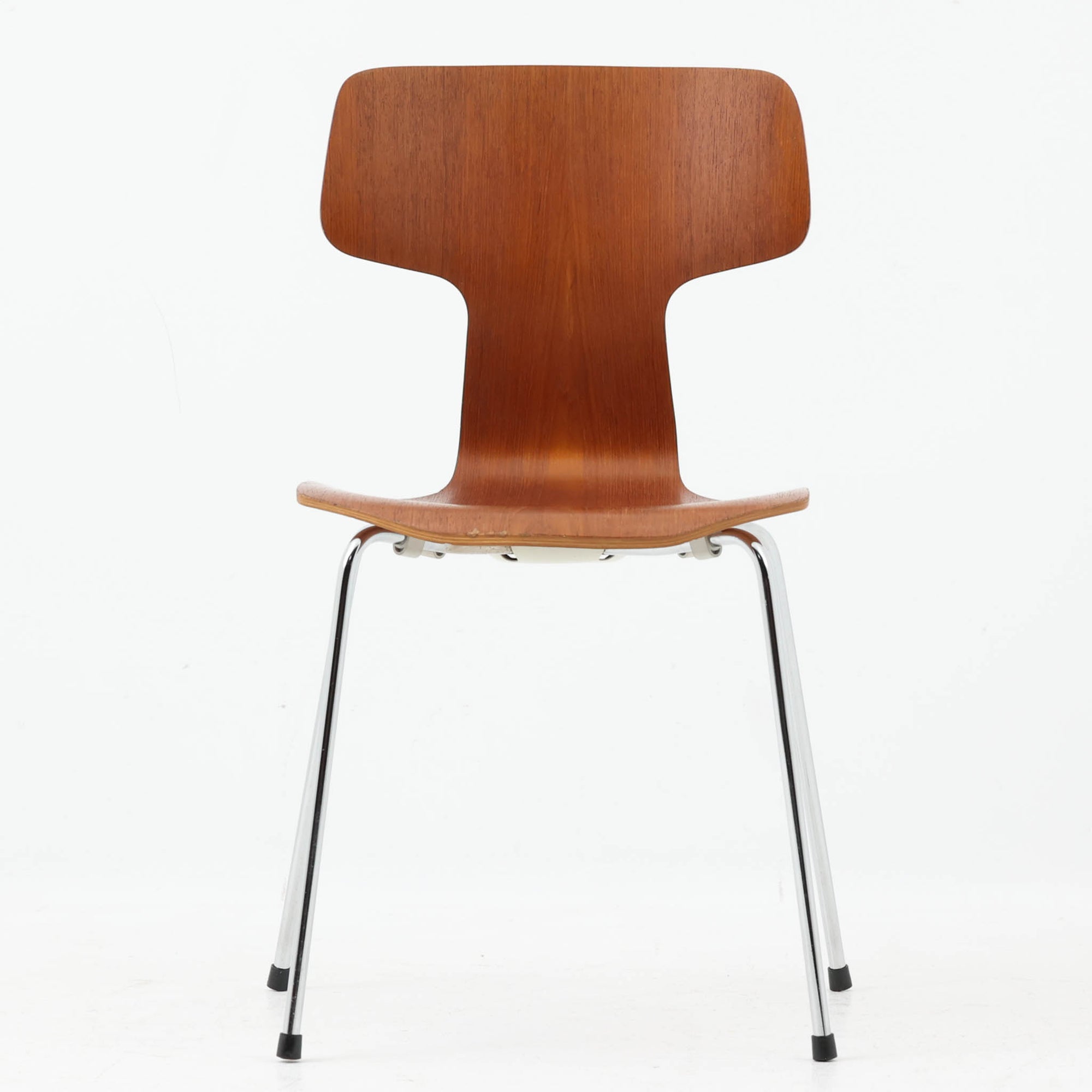 アルネ・ヤコブセンがデザインし、Fritz Hansenが製造した「T Chair」です。チーク材の成形合板による背座一体型のシェルは、背面上部を左右に広げた特徴的なシルエットと、身体に沿う緩やかな曲面が魅力。細身の金属脚との組み合わせが軽快で、ダイニングはもちろん、書斎や玄関のアクセントチェアにもおすすめです。美しい木目と時を重ねた風合い、合理的な構造に宿る北欧ビンテージらしい存在感を楽しめます。