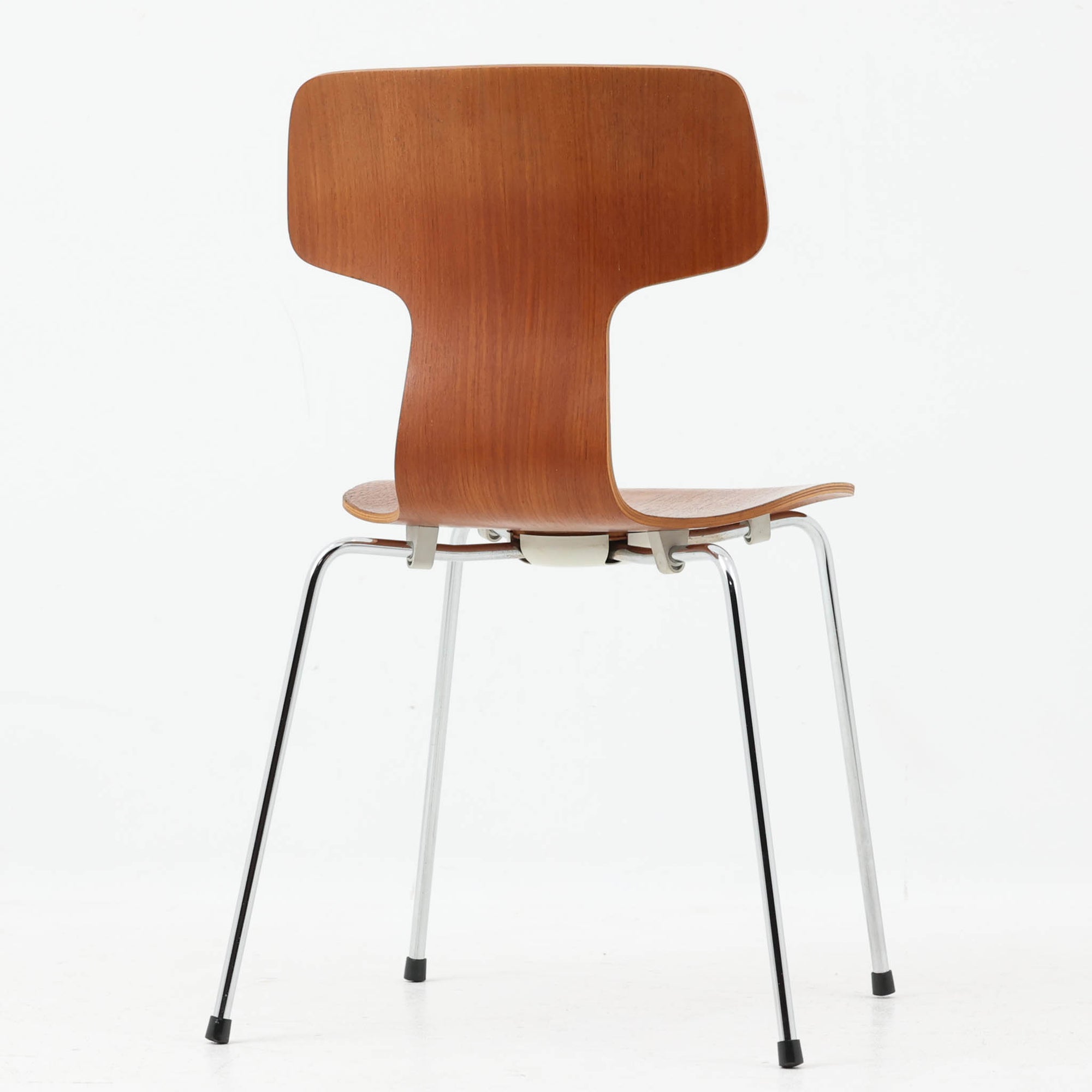 アルネ・ヤコブセンがデザインし、Fritz Hansenが製造した「T Chair」です。チーク材の成形合板による背座一体型のシェルは、背面上部を左右に広げた特徴的なシルエットと、身体に沿う緩やかな曲面が魅力。細身の金属脚との組み合わせが軽快で、ダイニングはもちろん、書斎や玄関のアクセントチェアにもおすすめです。美しい木目と時を重ねた風合い、合理的な構造に宿る北欧ビンテージらしい存在感を楽しめます。