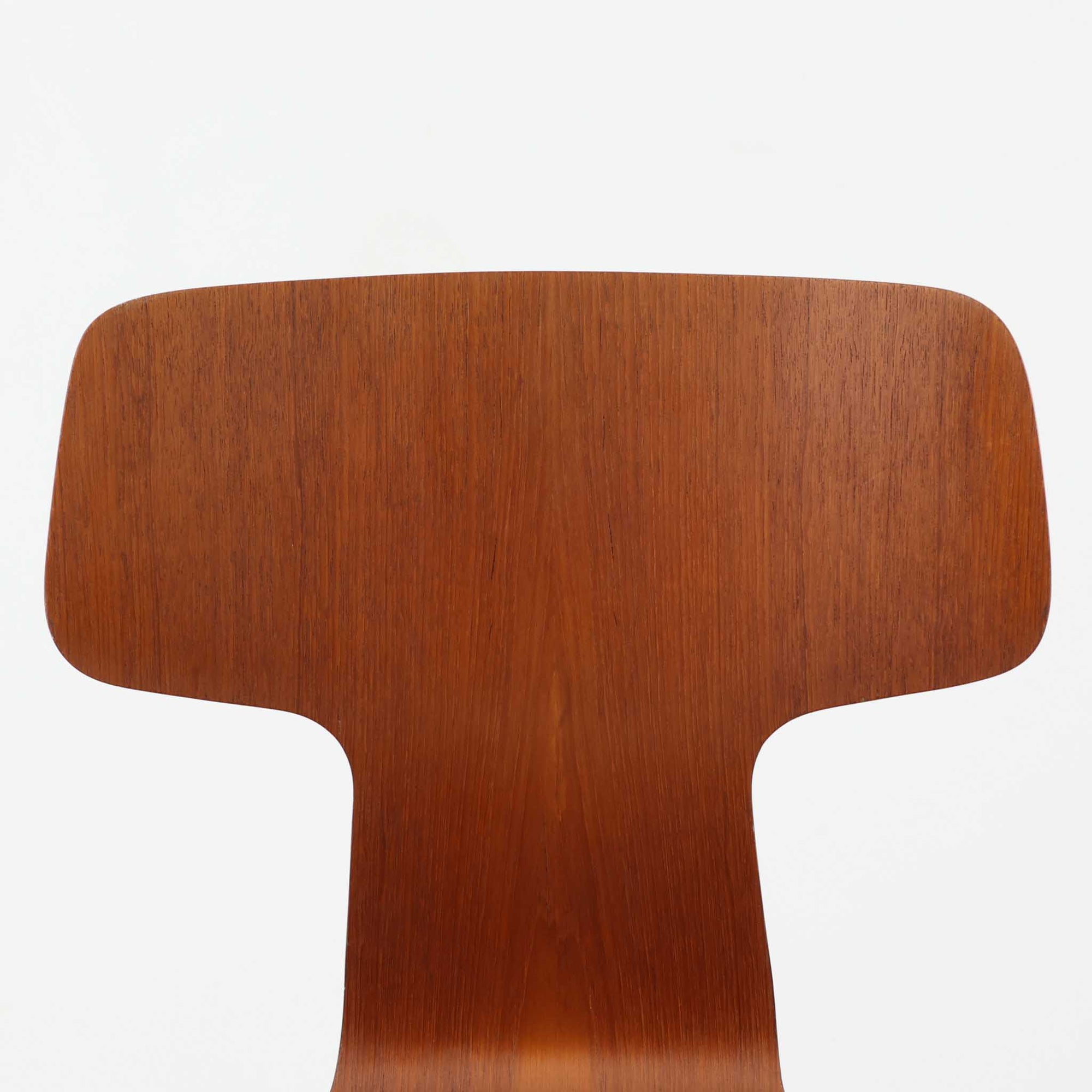 アルネ・ヤコブセンがデザインし、Fritz Hansenが製造した「T Chair」です。チーク材の成形合板による背座一体型のシェルは、背面上部を左右に広げた特徴的なシルエットと、身体に沿う緩やかな曲面が魅力。細身の金属脚との組み合わせが軽快で、ダイニングはもちろん、書斎や玄関のアクセントチェアにもおすすめです。美しい木目と時を重ねた風合い、合理的な構造に宿る北欧ビンテージらしい存在感を楽しめます。